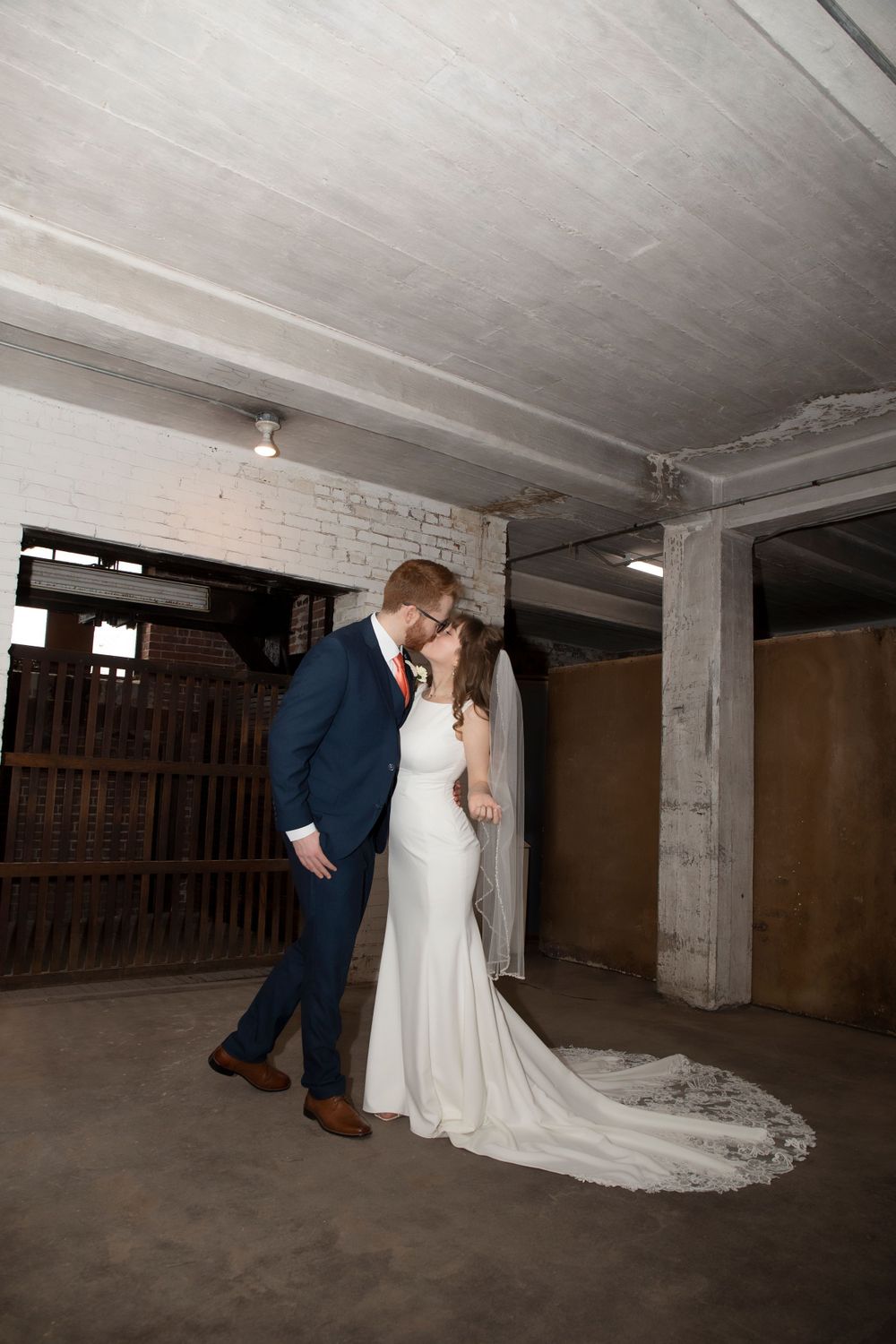 A romantic wedding couple share an intimate moment in an industrial space with brick walls and concrete floors.