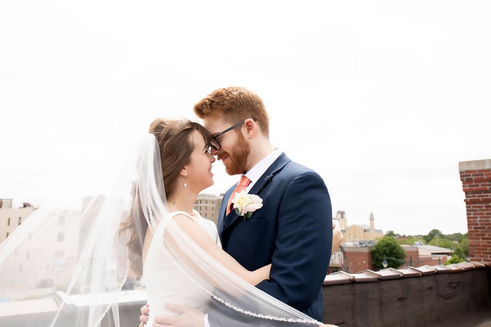 A tender moment between newlyweds with flowing veil against an urban rooftop backdrop.