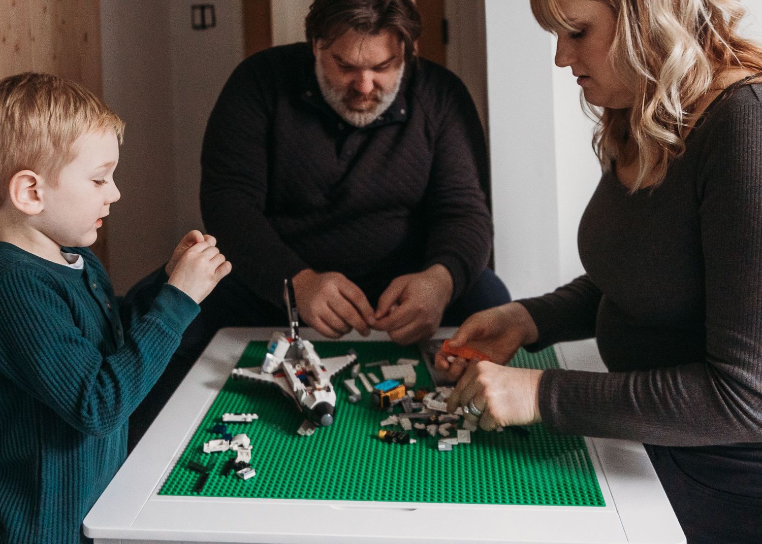 People playing with LEGO pieces on a green baseplate at a table.