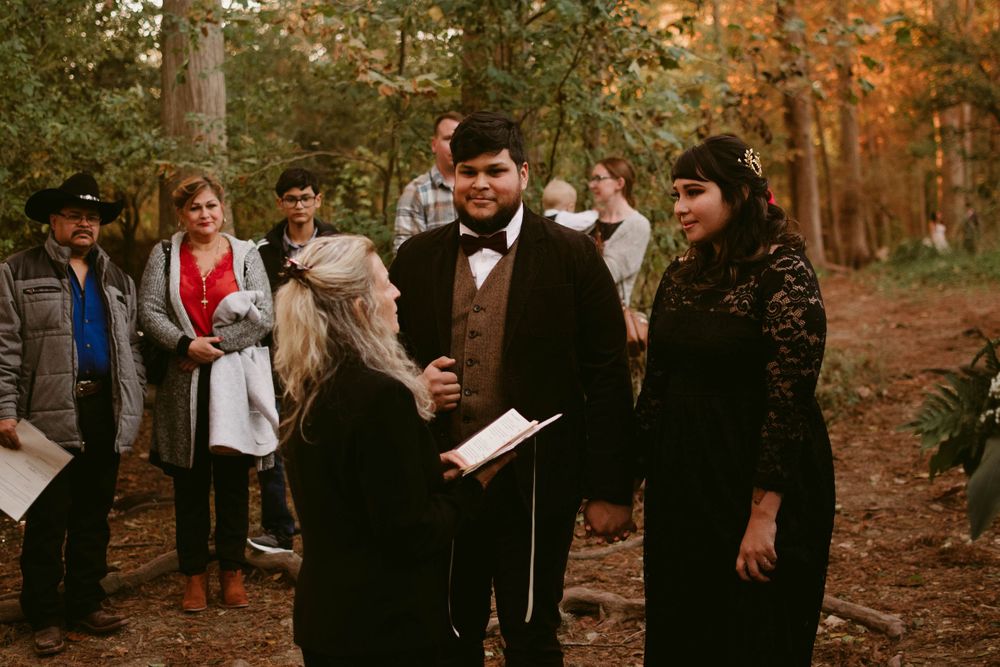 A wedding ceremony takes place on a forest trail with guests watching.