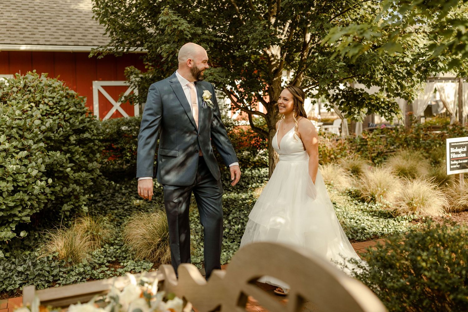 Outdoor first look wedding moment with red barn in garden setting.