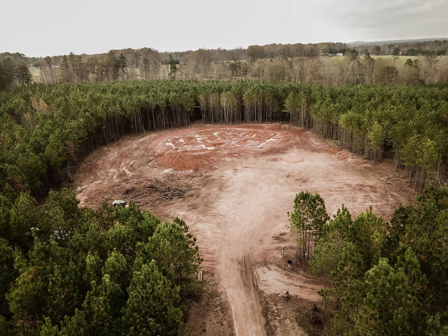 Aerial view of a cleared circular construction site surrounded by dense pine forest.