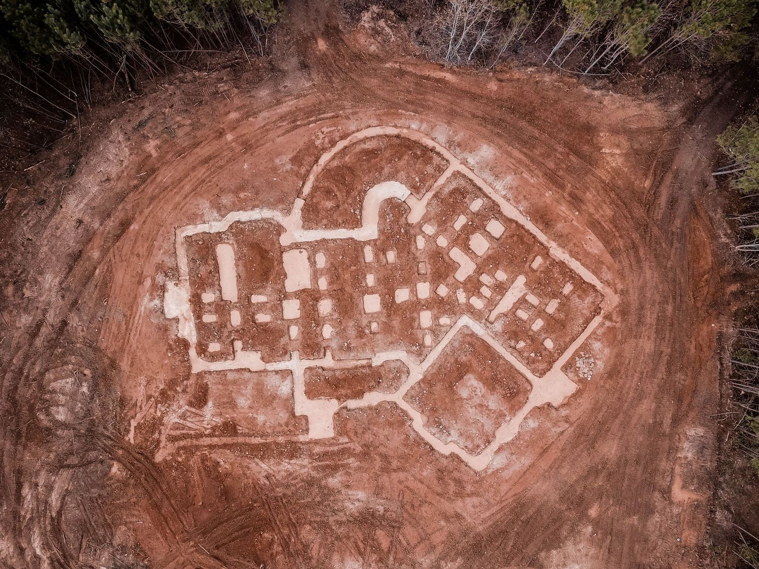 Overhead view of residential foundation outline on cleared red dirt with detailed room divisions.