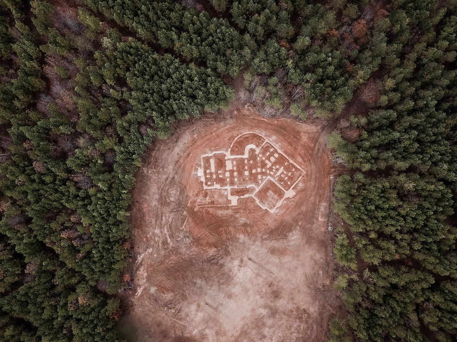 Aerial drone photograph of a house foundation outline in a forest clearing.
