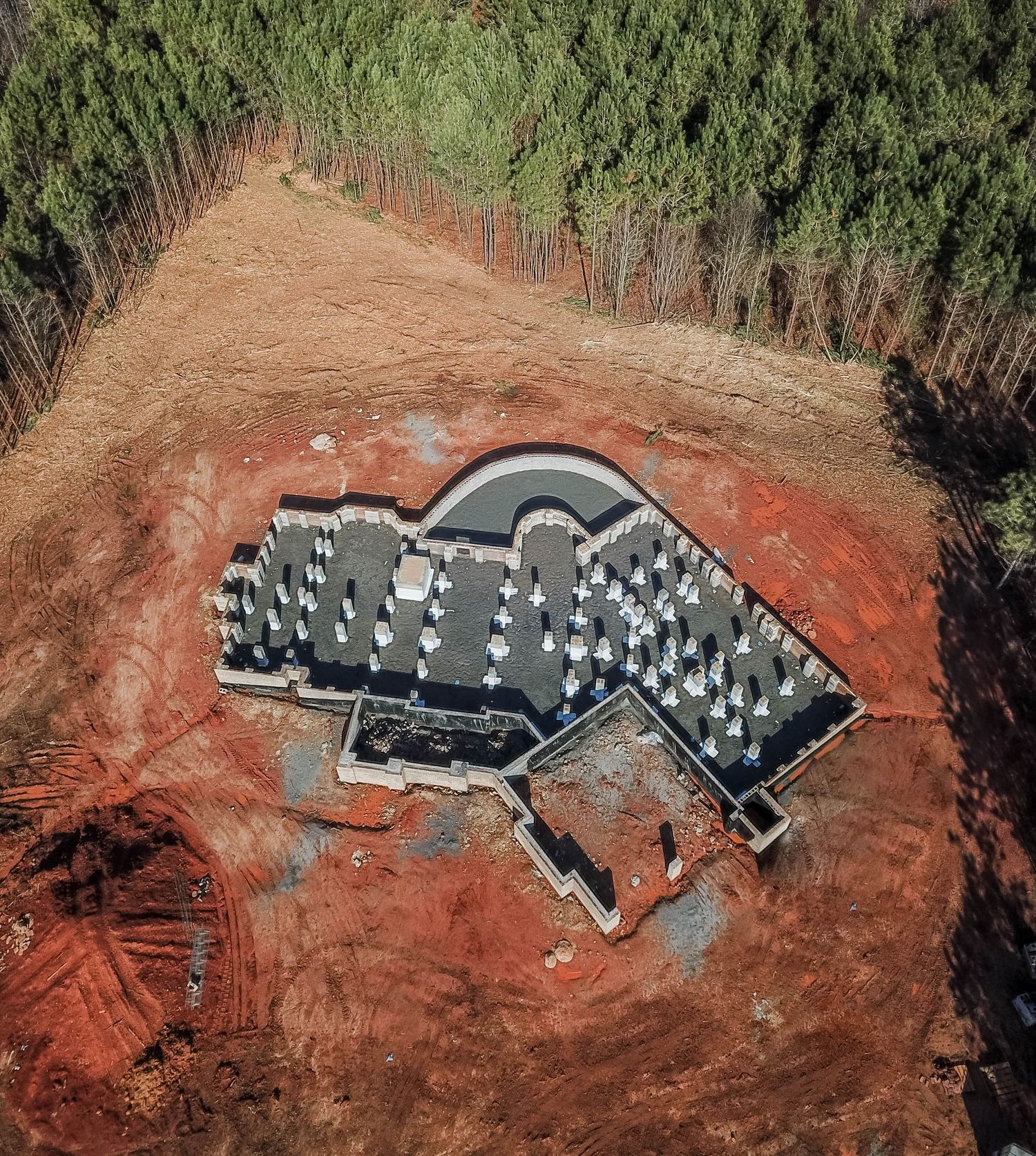 Overhead view of concrete foundation with vertical supports being constructed in a cleared forest area.
