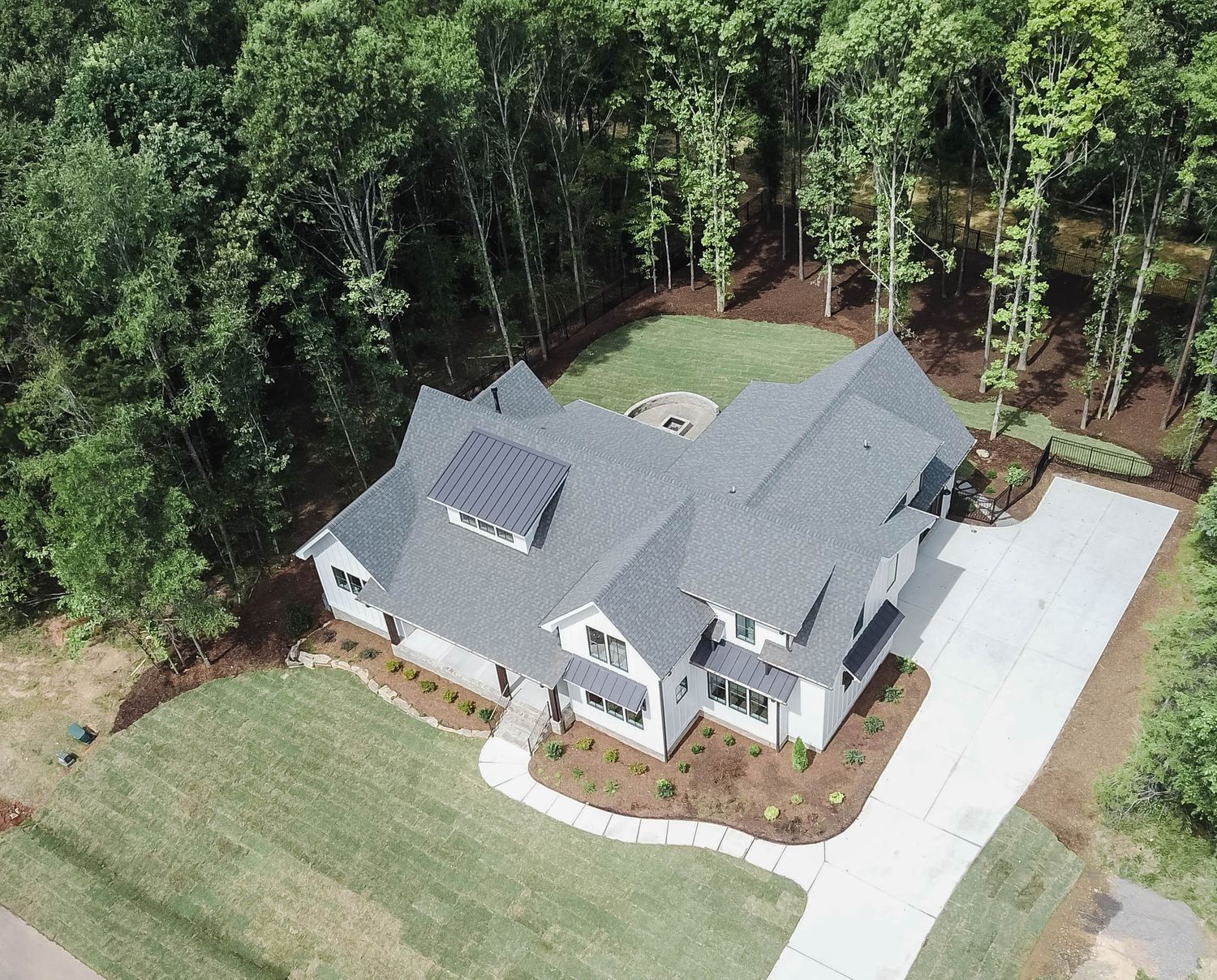 Aerial view of large white modern farmhouse with grey roof and curved driveway.