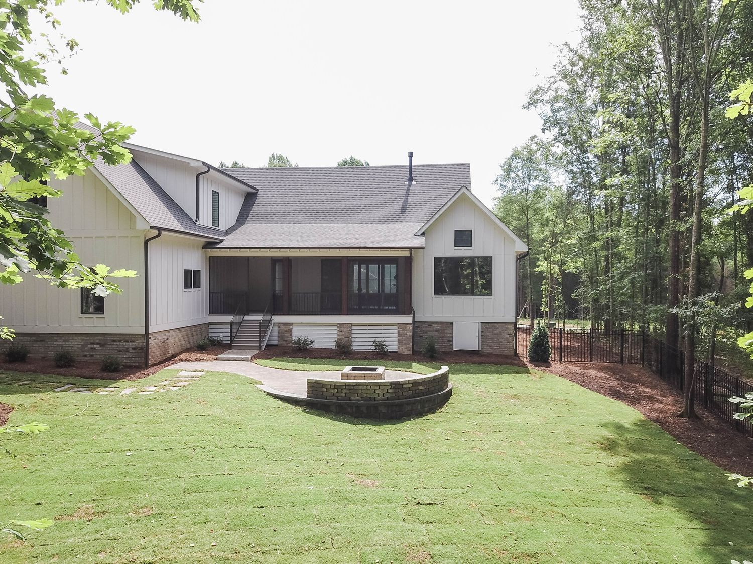 Rear view of white modern home featuring covered porch and circular stone fire pit.