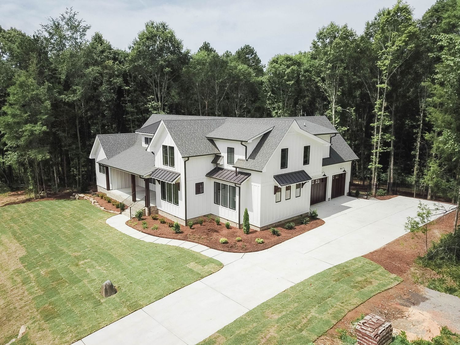 Aerial view of modern white farmhouse with black trim and curved concrete driveway.