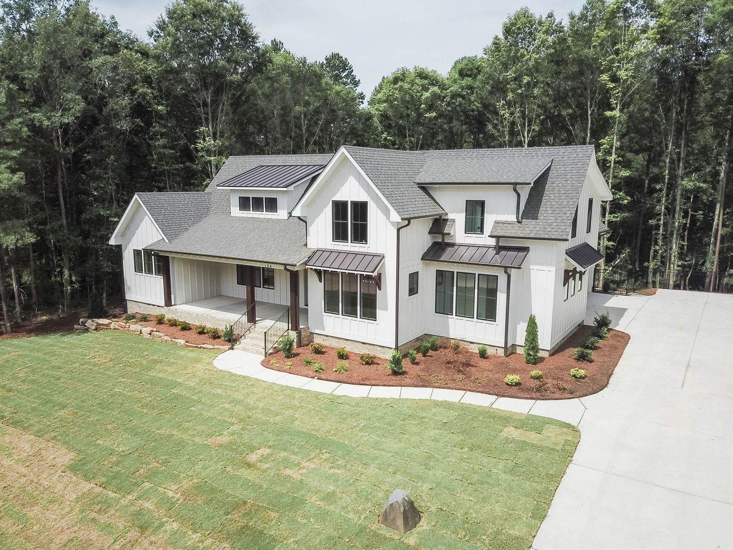 Modern white farmhouse with black trim and multiple dormers surrounded by fresh landscaping.