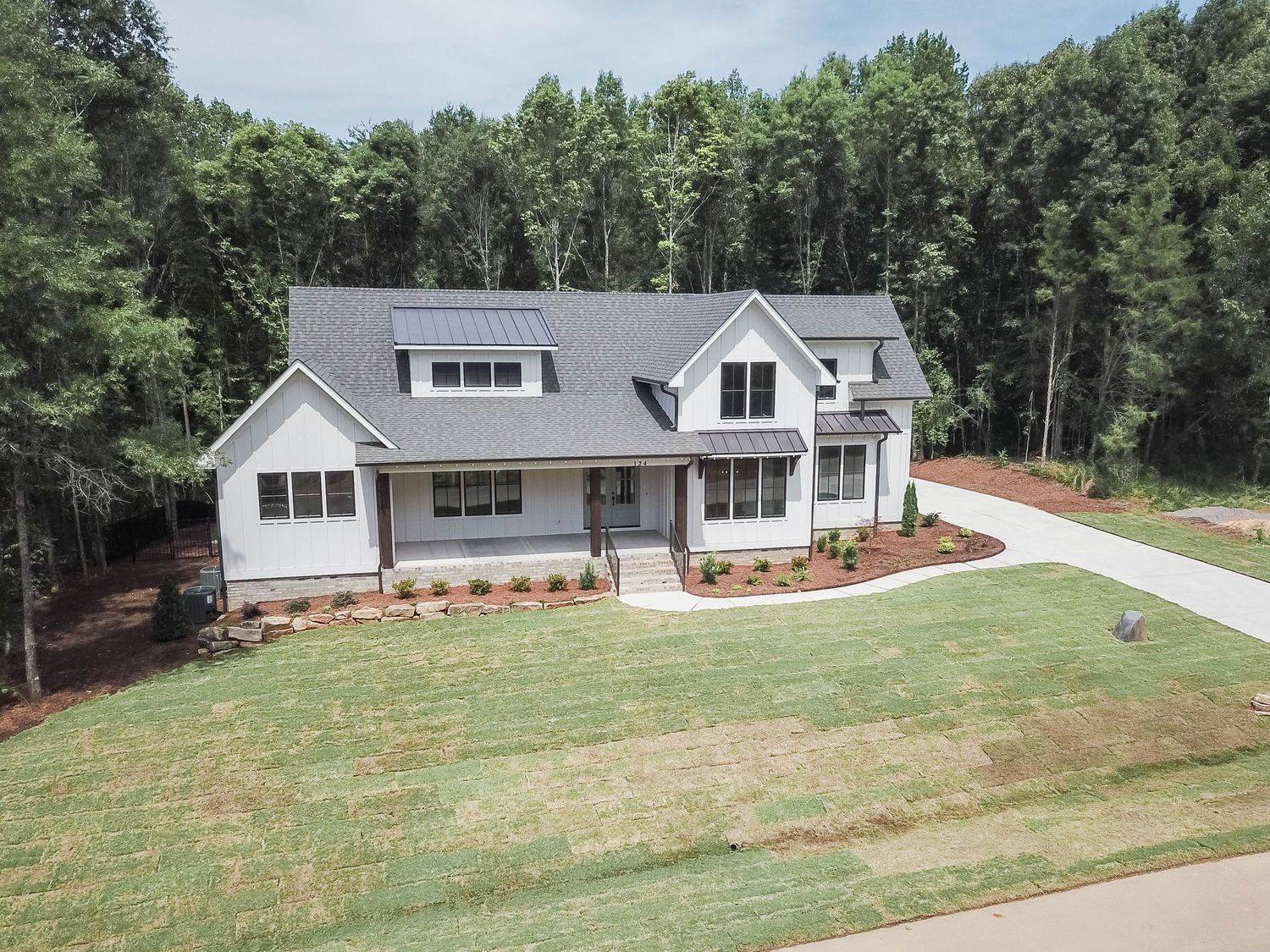 Modern farmhouse style home with white exterior and grey roof nestled among trees with manicured lawn and curved driveway.
