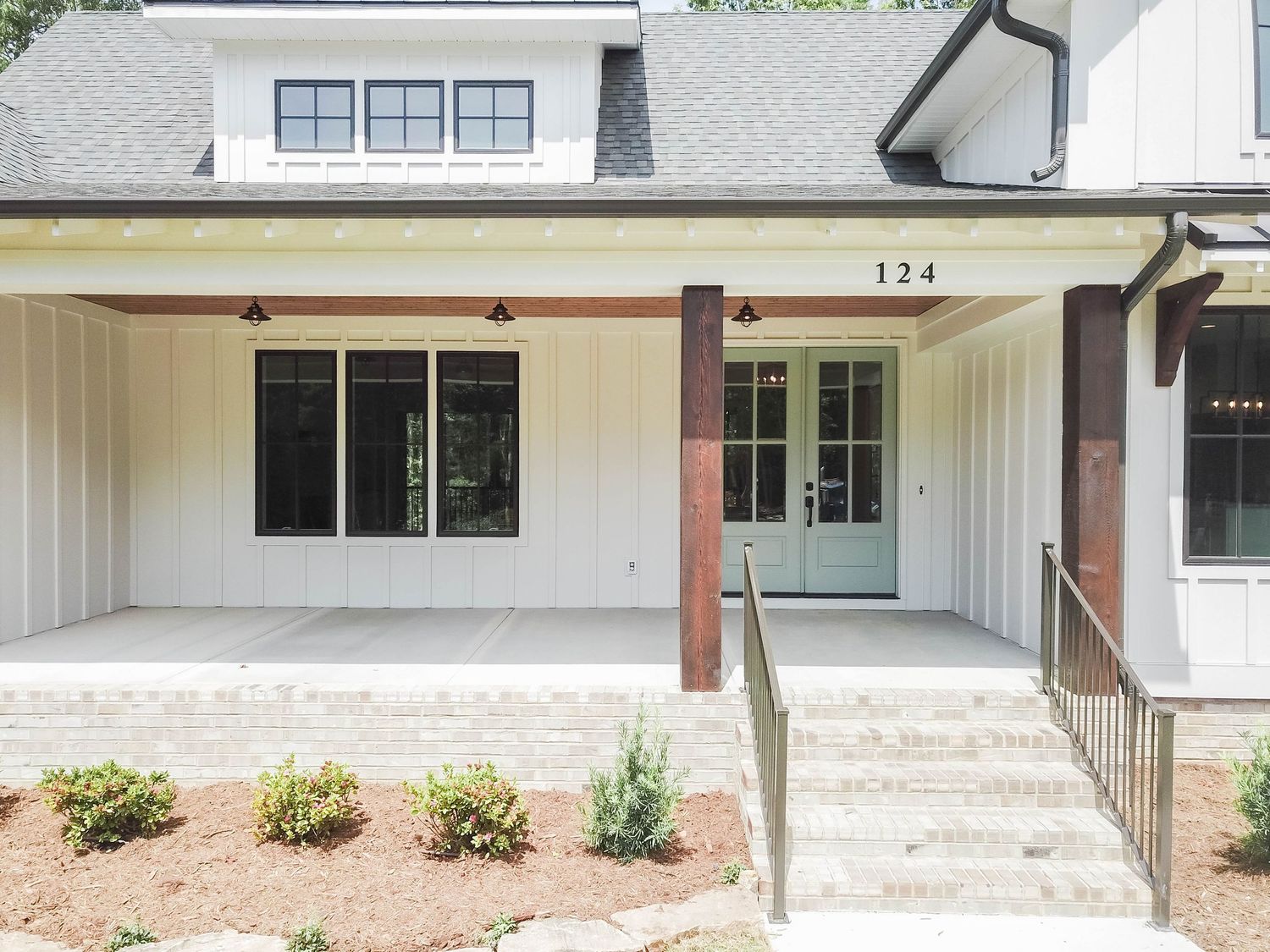 Front entrance of modern home featuring covered porch with white columns and contemporary house numbers.