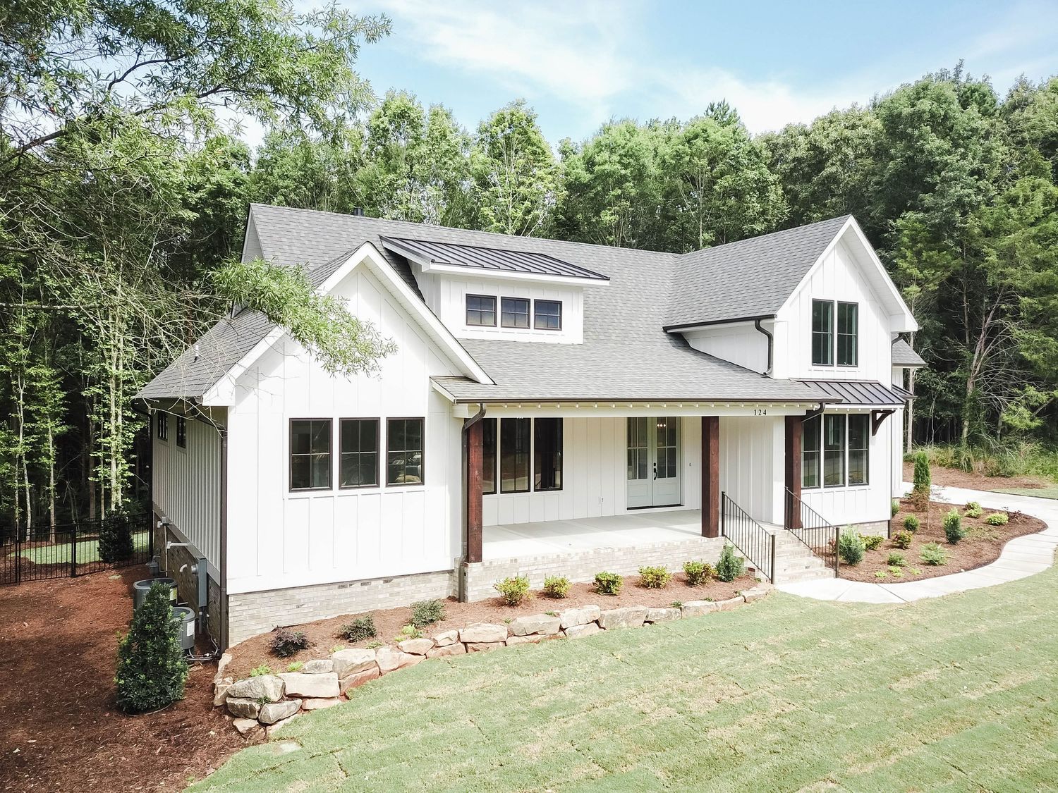 Contemporary white farmhouse with wraparound porch and modern architectural details.