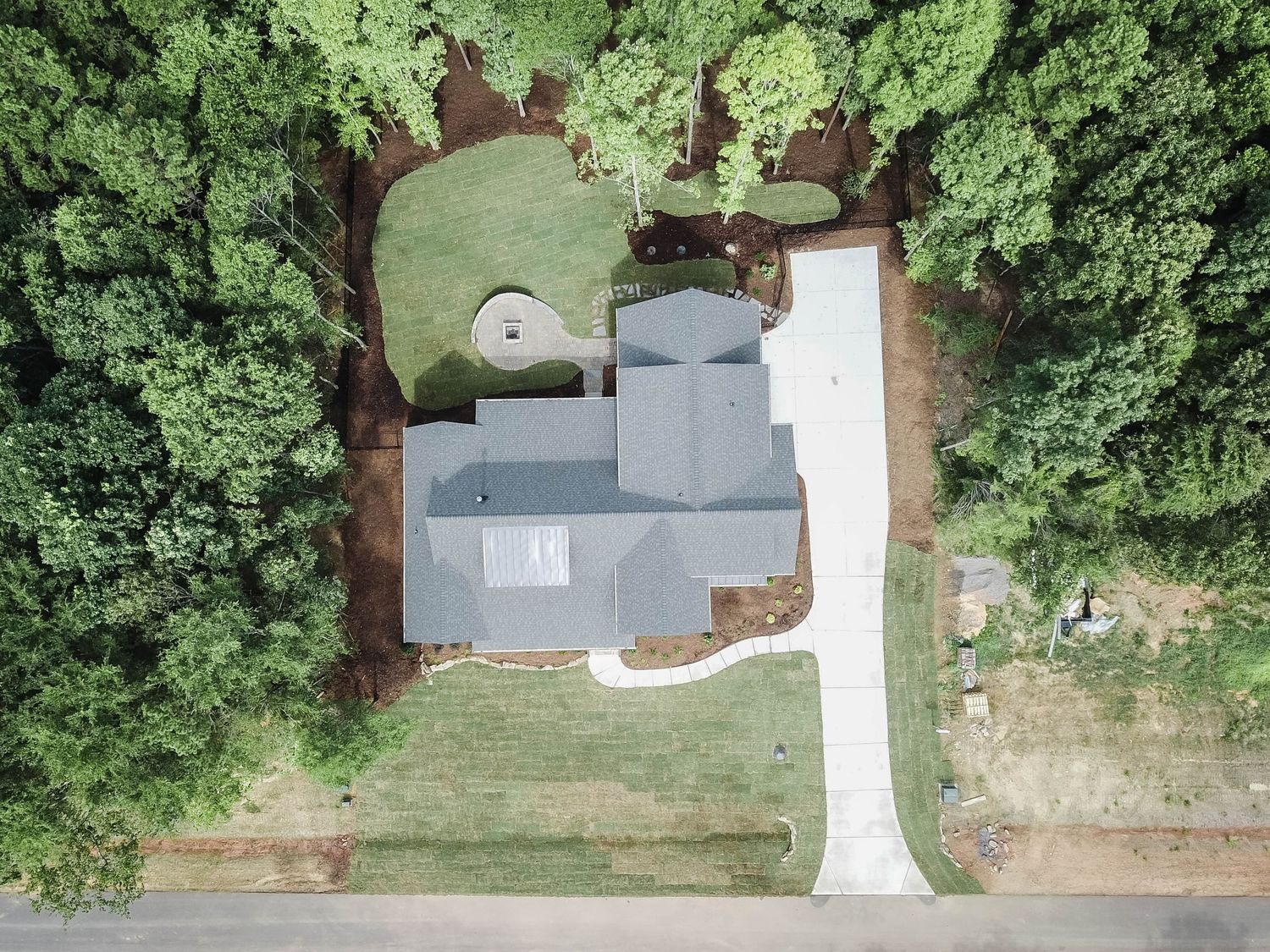 Aerial view of a white modern farmhouse with circular driveway surrounded by trees.