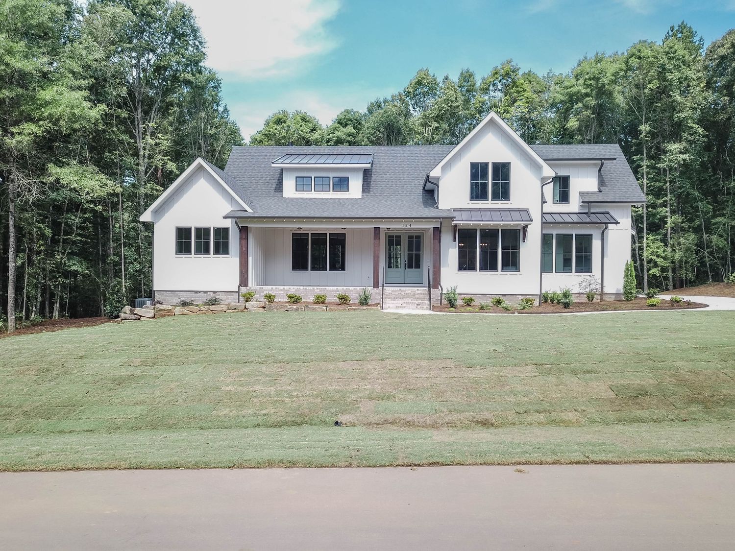 Front view of a spacious modern farmhouse with multiple dormers and clean white siding.
