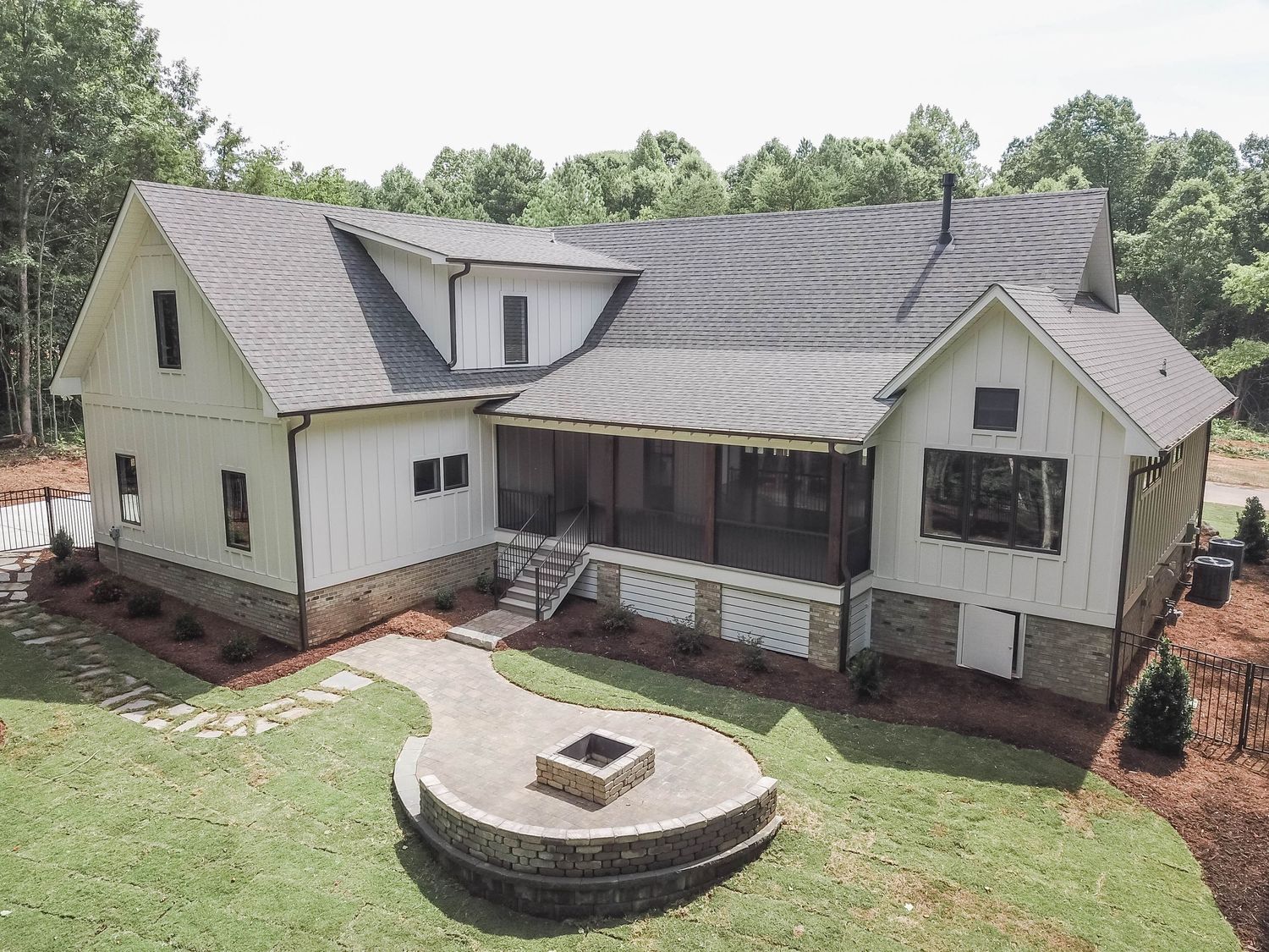 Modern farmhouse style home with white exterior and circular stone fire pit patio in backyard.