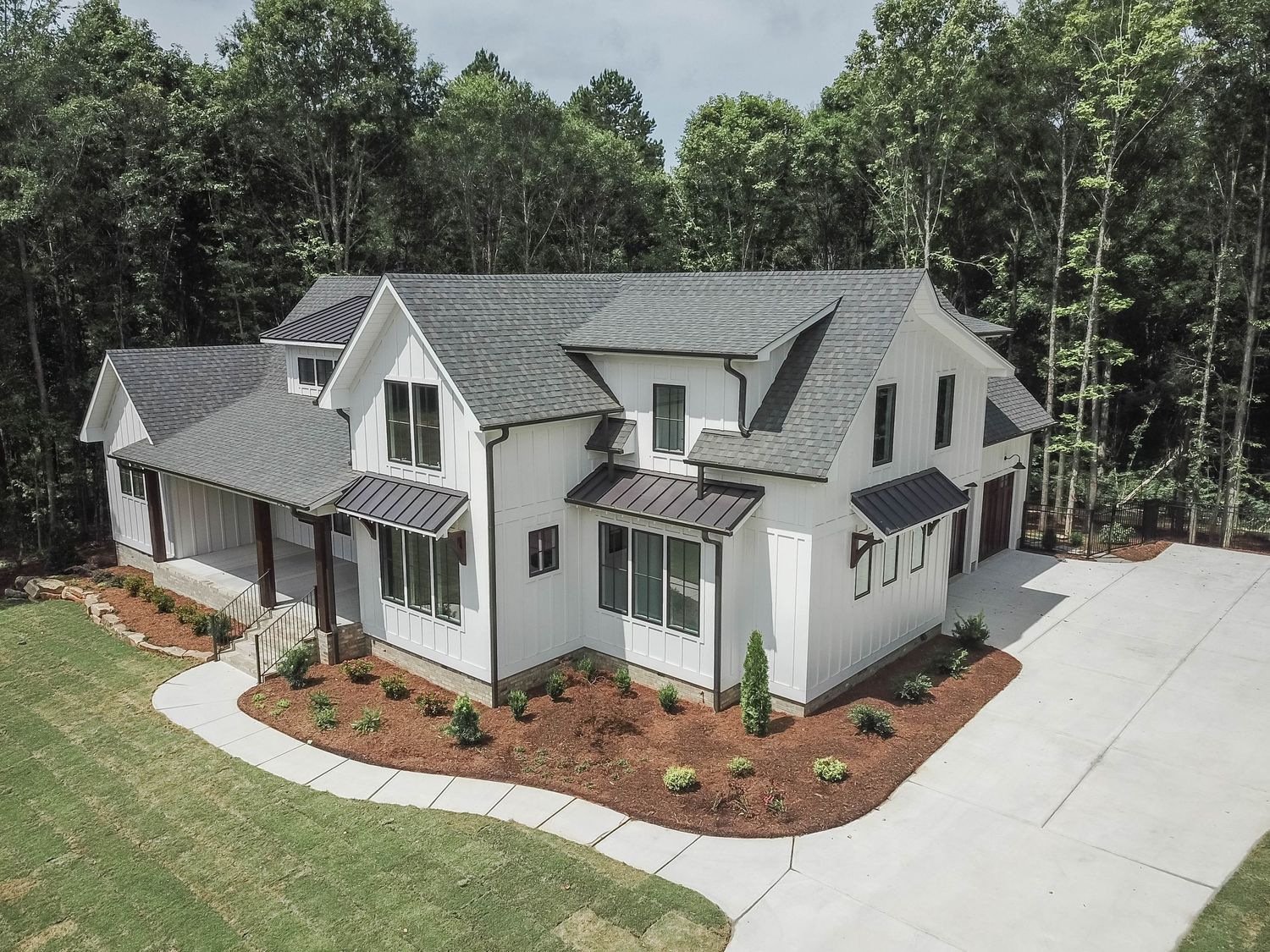 Drone shot of a modern white farmhouse featuring metal roof accents and professional landscaping.