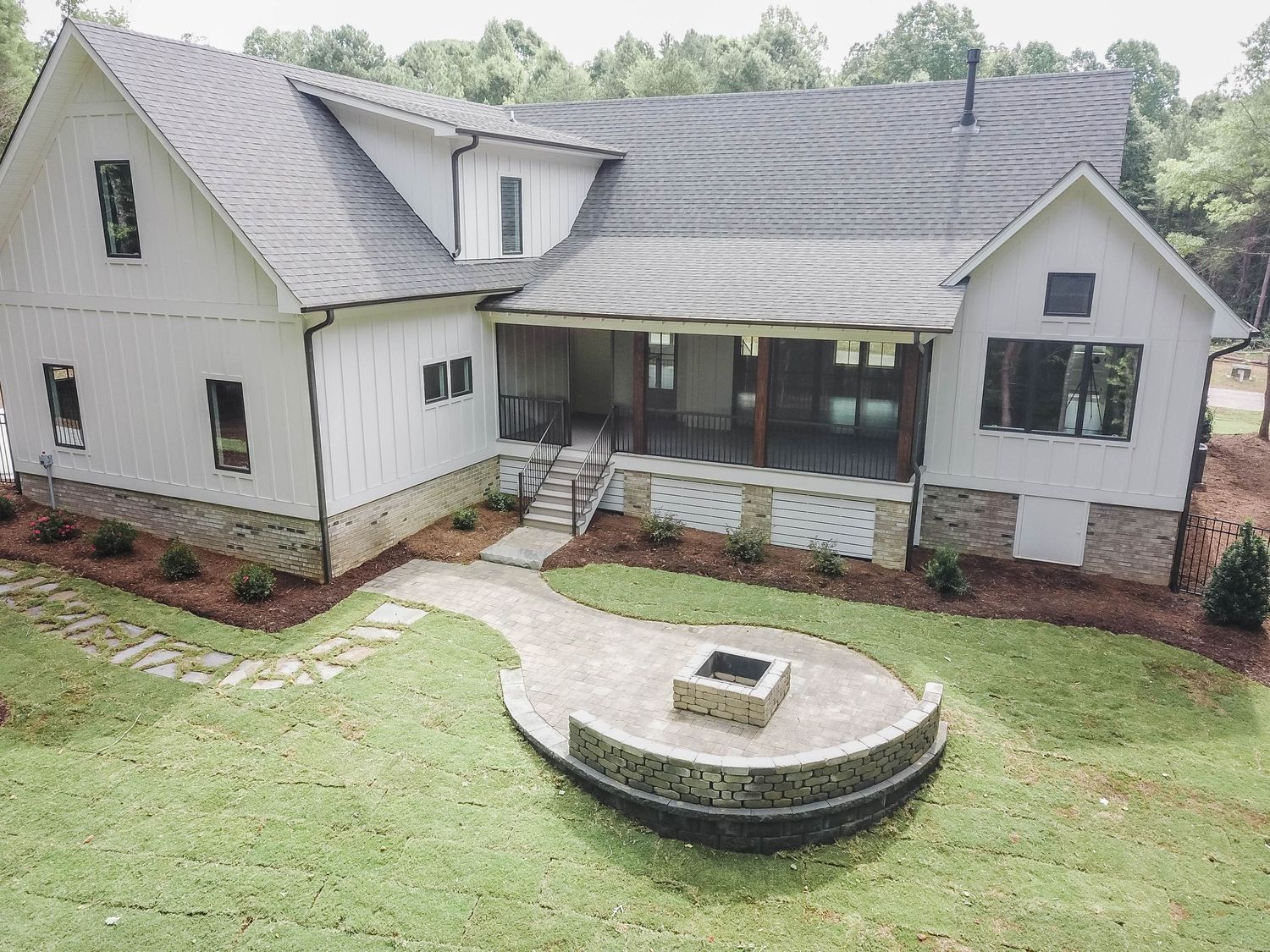 White farmhouse with covered porch and circular stone fire pit feature viewed from rear angle.