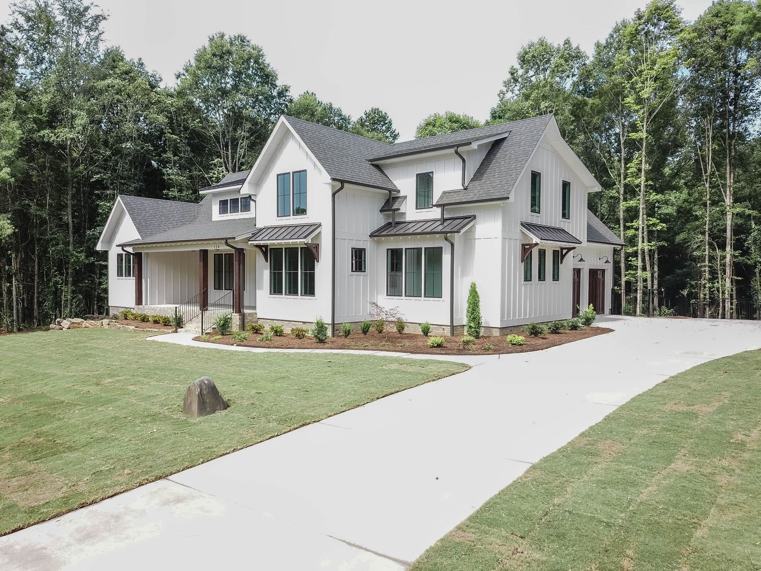 Modern white farmhouse with dormer windows and covered front porch surrounded by landscaped lawn.