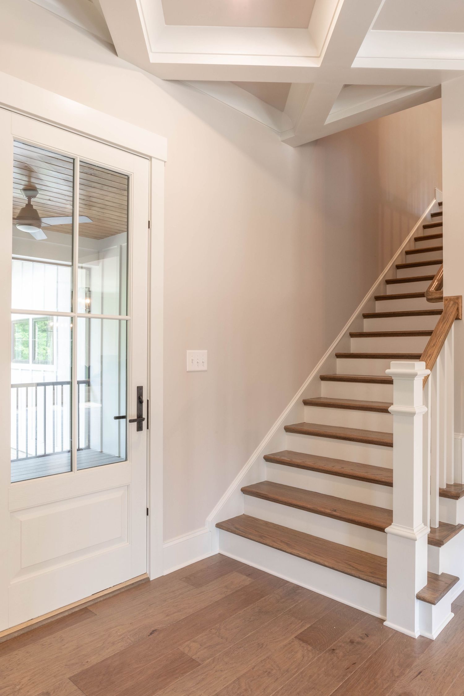 Interior staircase with wooden treads, white risers, and modern white railings beside a glass door entrance.