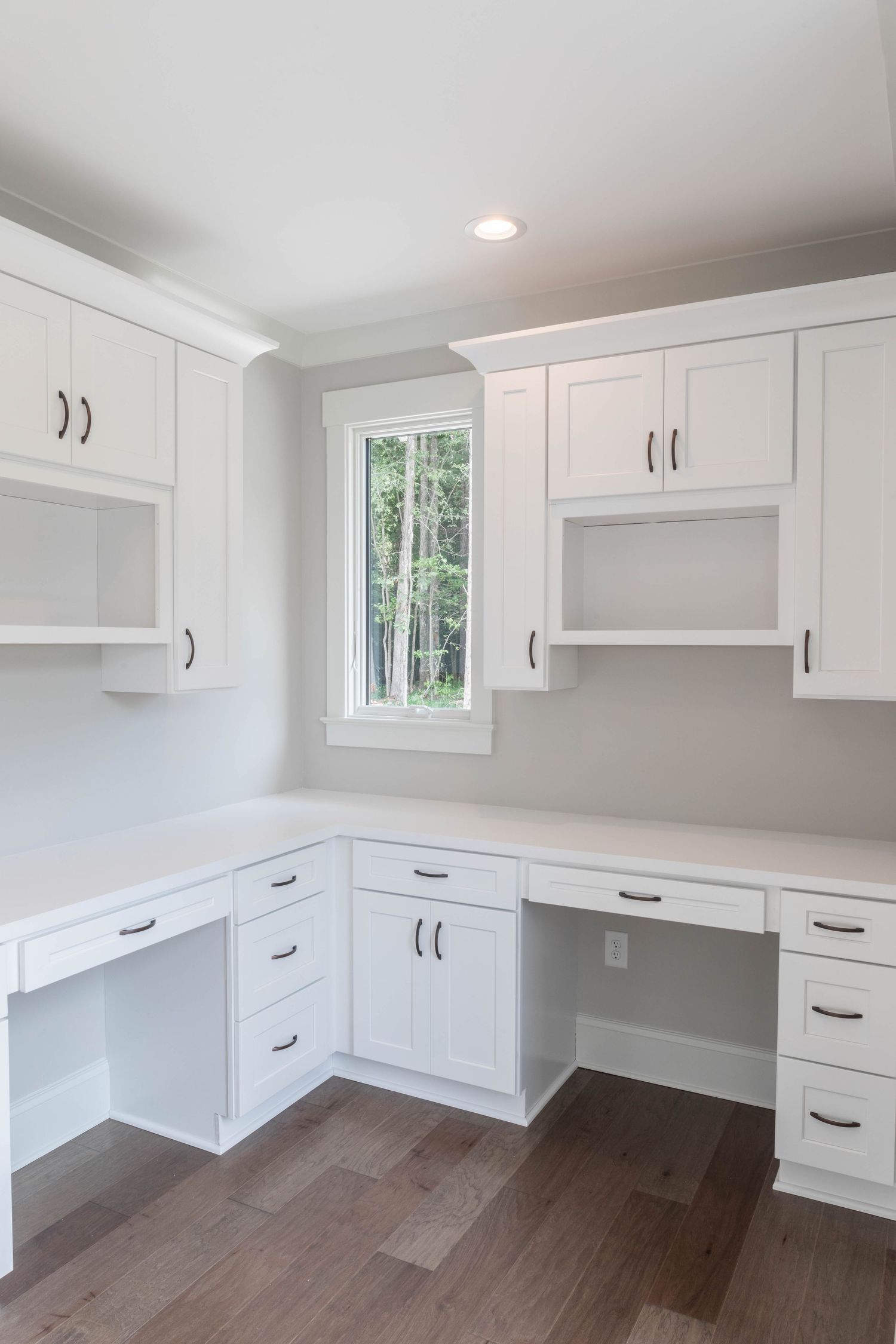 Custom white home office with L-shaped desk, built-in cabinets, and natural light from window.