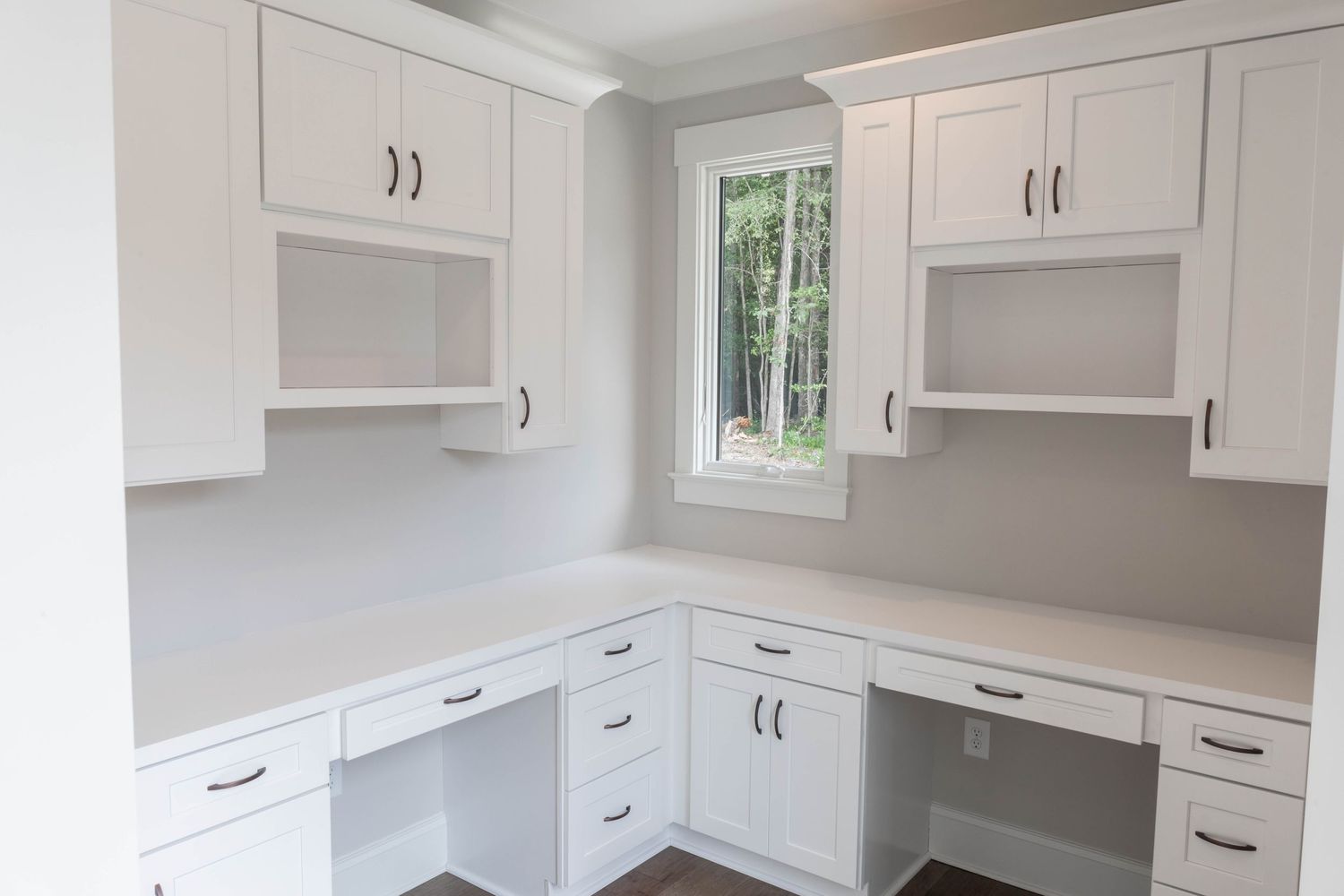 White built-in office space with L-shaped desk, window, and multiple storage cabinets.