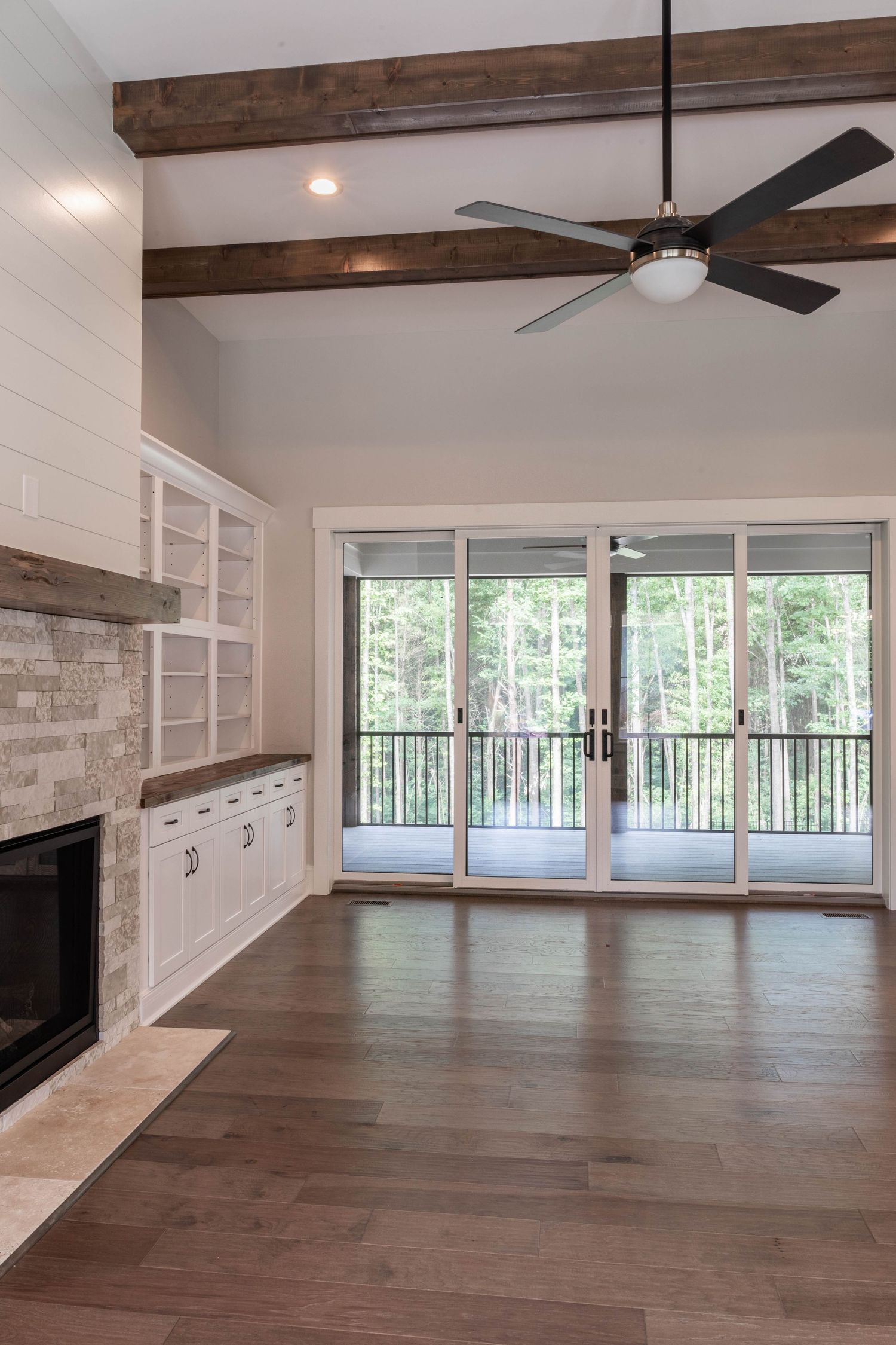 Living room with exposed wood beams, built-in storage, stone fireplace and sliding glass doors to deck.