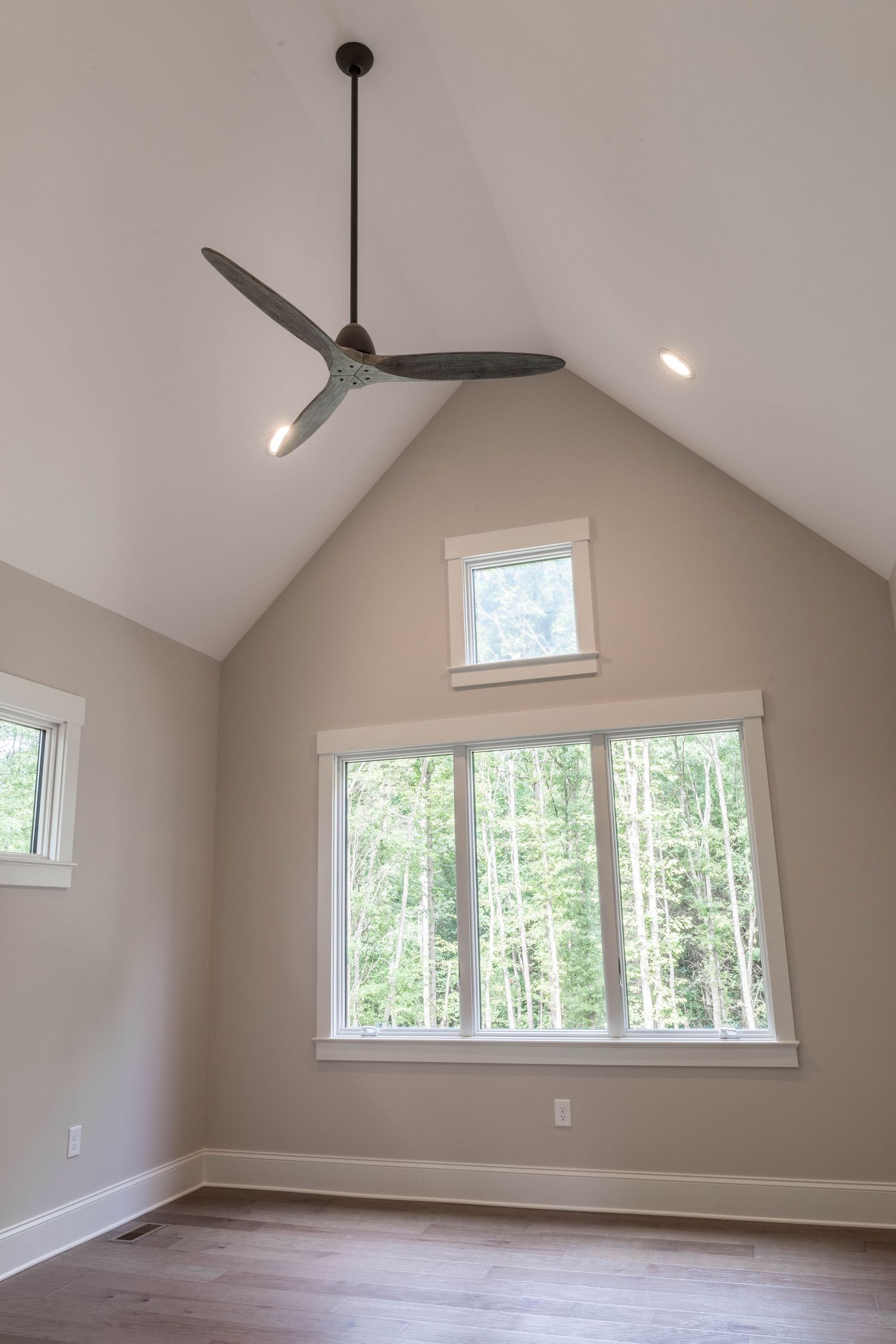 Vaulted ceiling room with modern ceiling fan, large windows, and natural light.