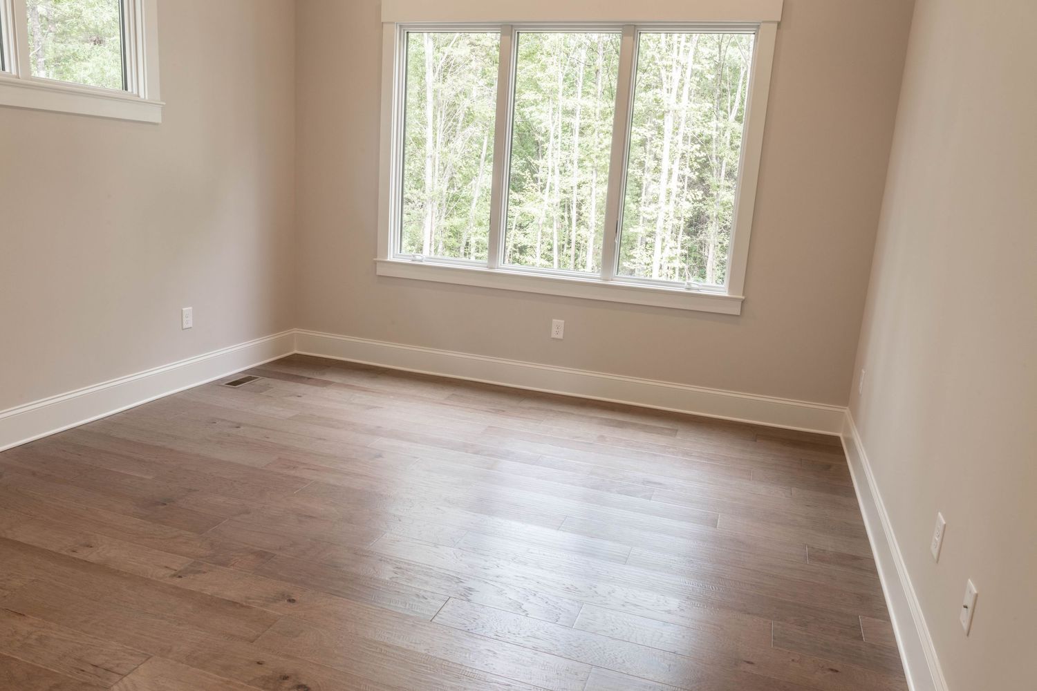 Modern bedroom with hardwood floors, large windows and natural light showcasing a wooded view outside.