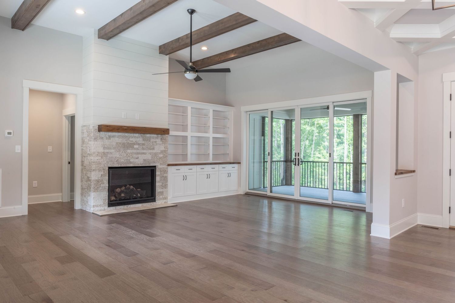 Open concept living room with exposed wooden beams, stone fireplace, and large windows overlooking natural scenery.