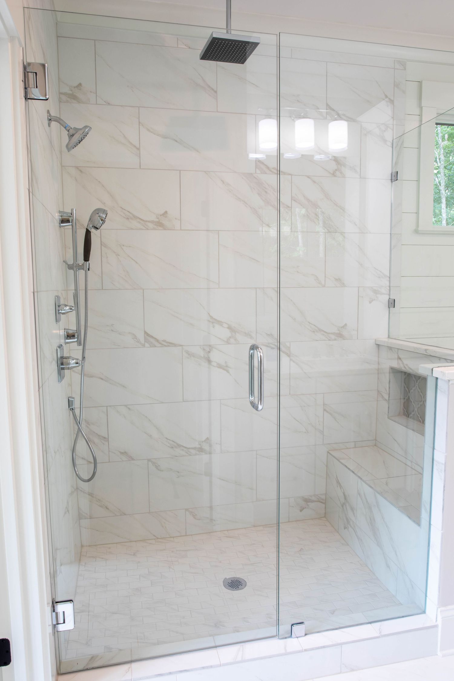 Spacious glass-enclosed marble shower with built-in bench and multiple shower heads.