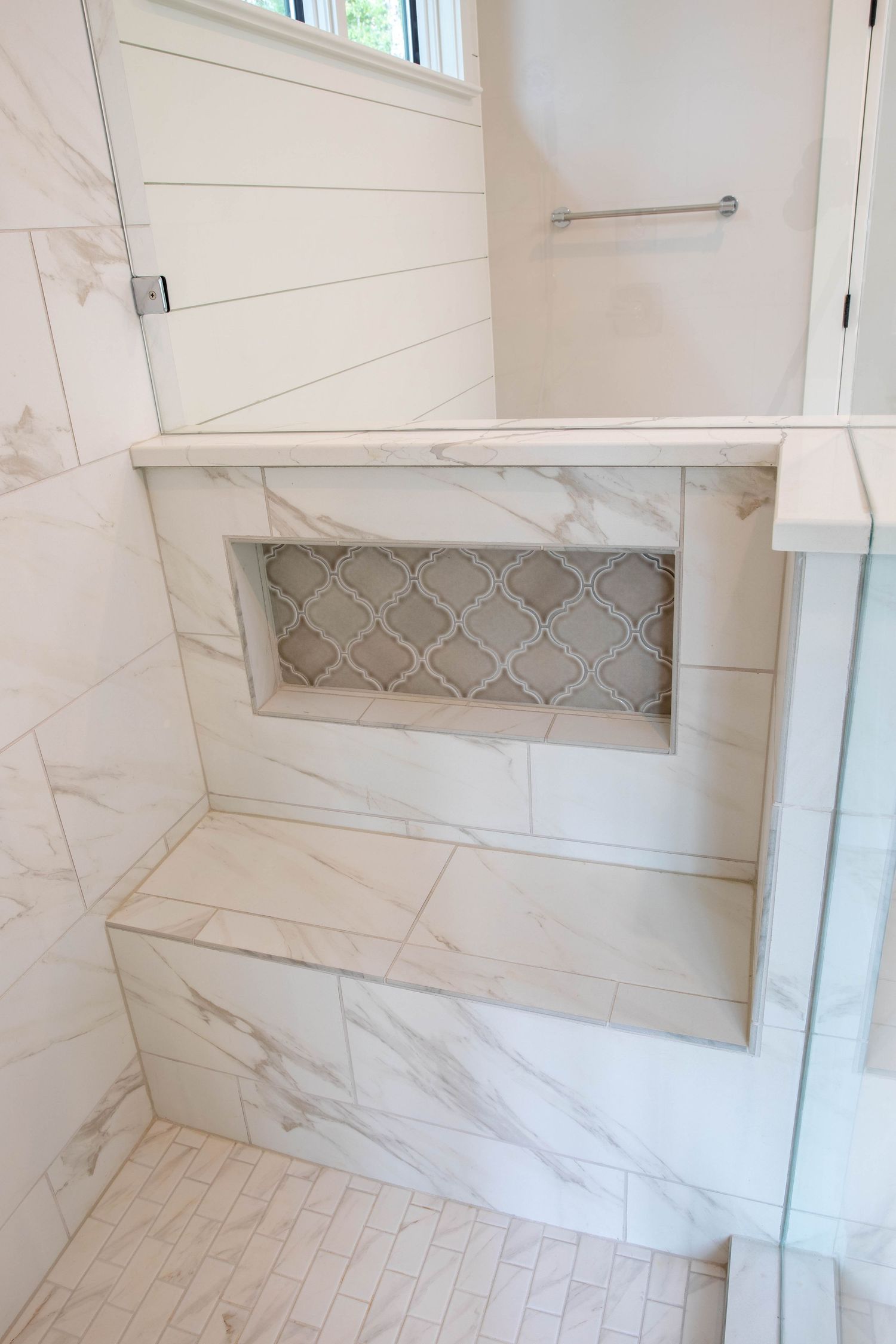 Marble shower bench with decorative tile niche insert and glass enclosure.
