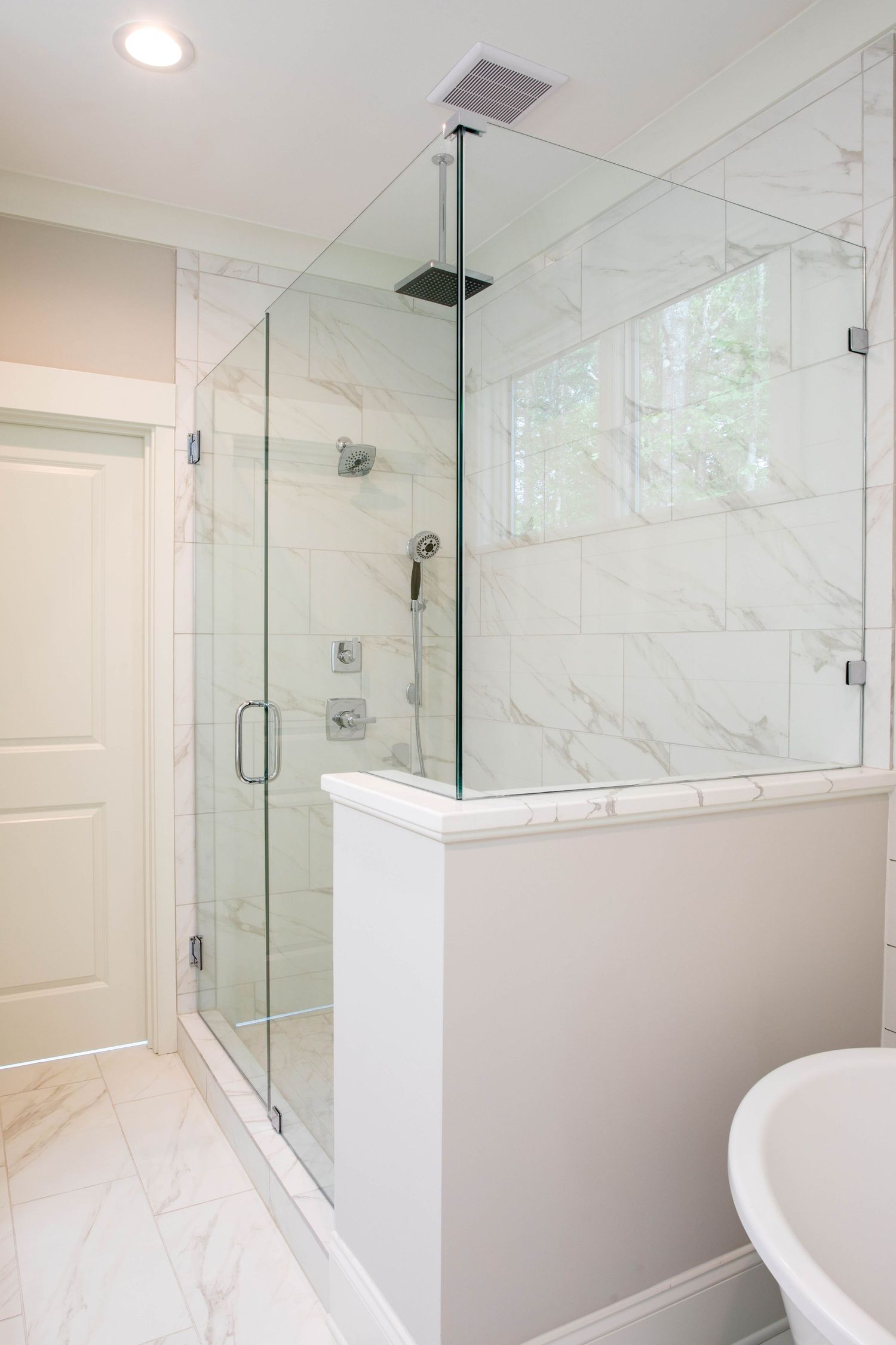 Modern glass shower enclosure with marble tile and rain showerhead in bright bathroom.