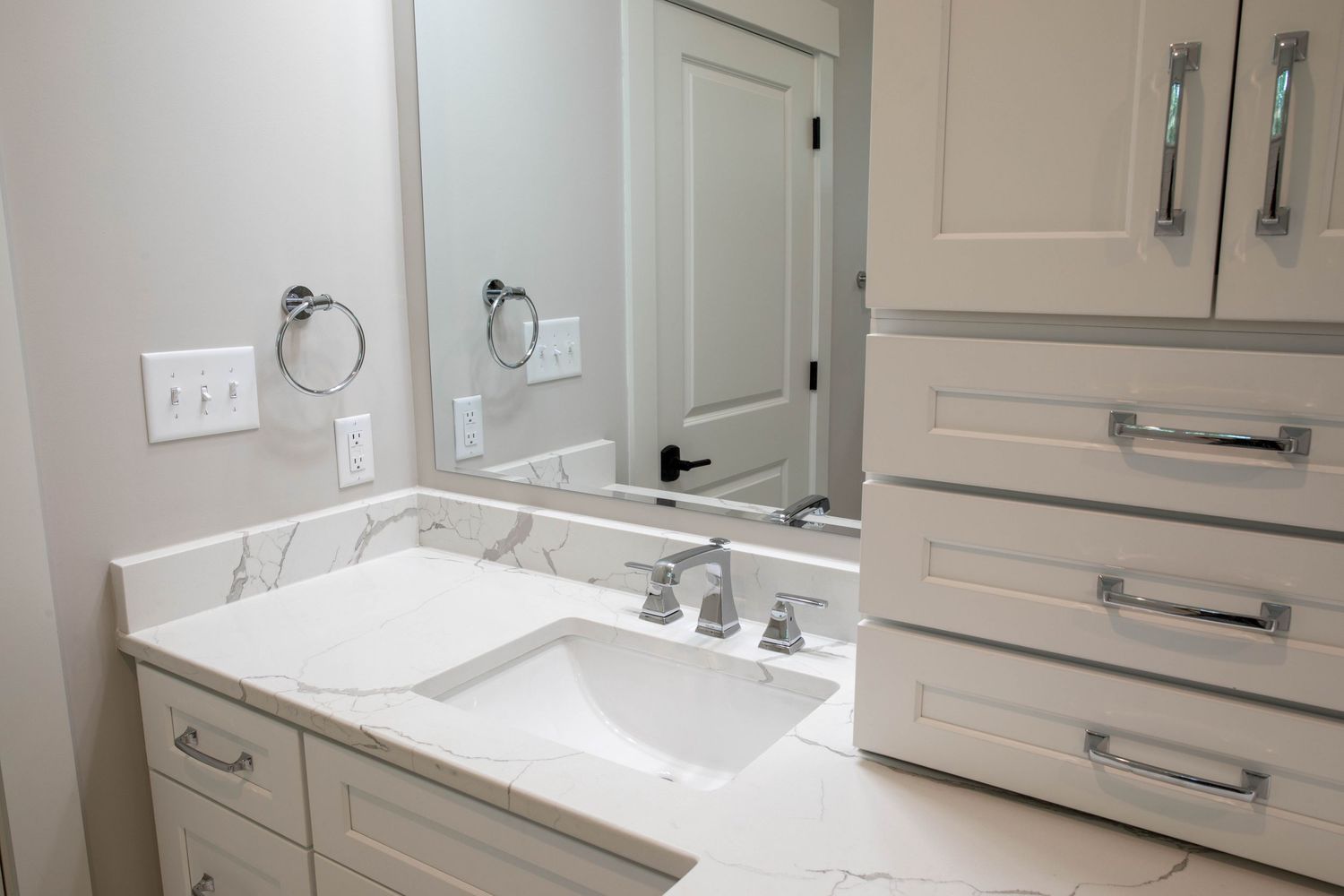 White vanity with marble countertop, chrome hardware, and framed mirror in a neutral bathroom.