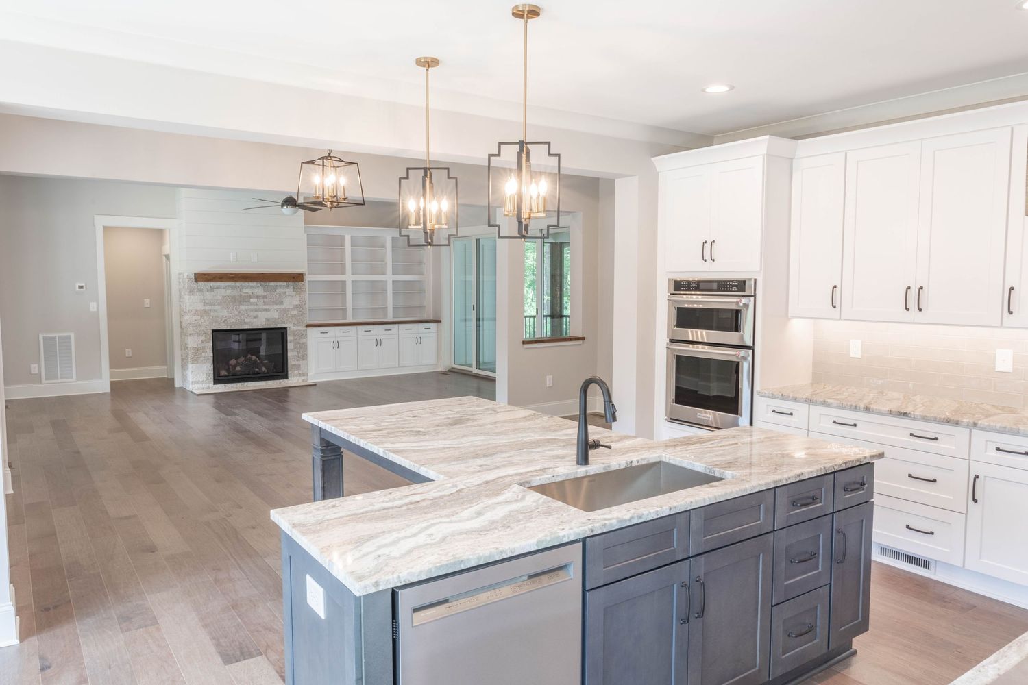 Luxurious modern kitchen with marble countertops, grey island, white cabinets and geometric pendant lighting.