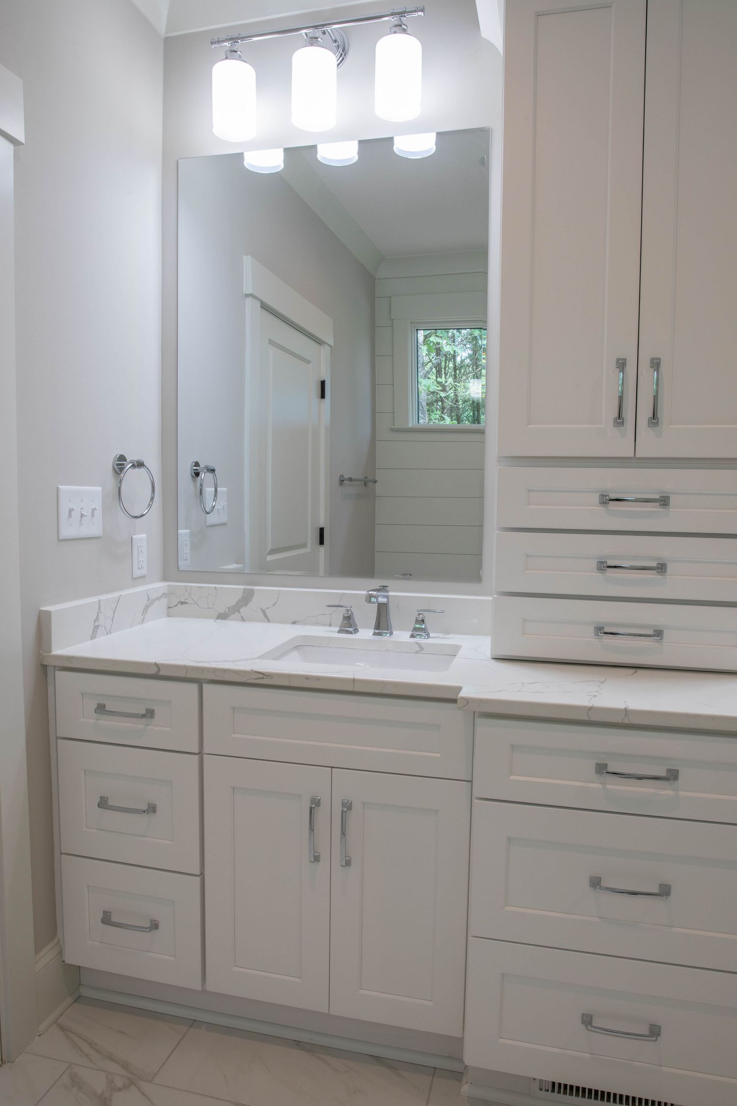 Elegant bathroom vanity with white cabinets, pendant lighting, and window letting in natural light.