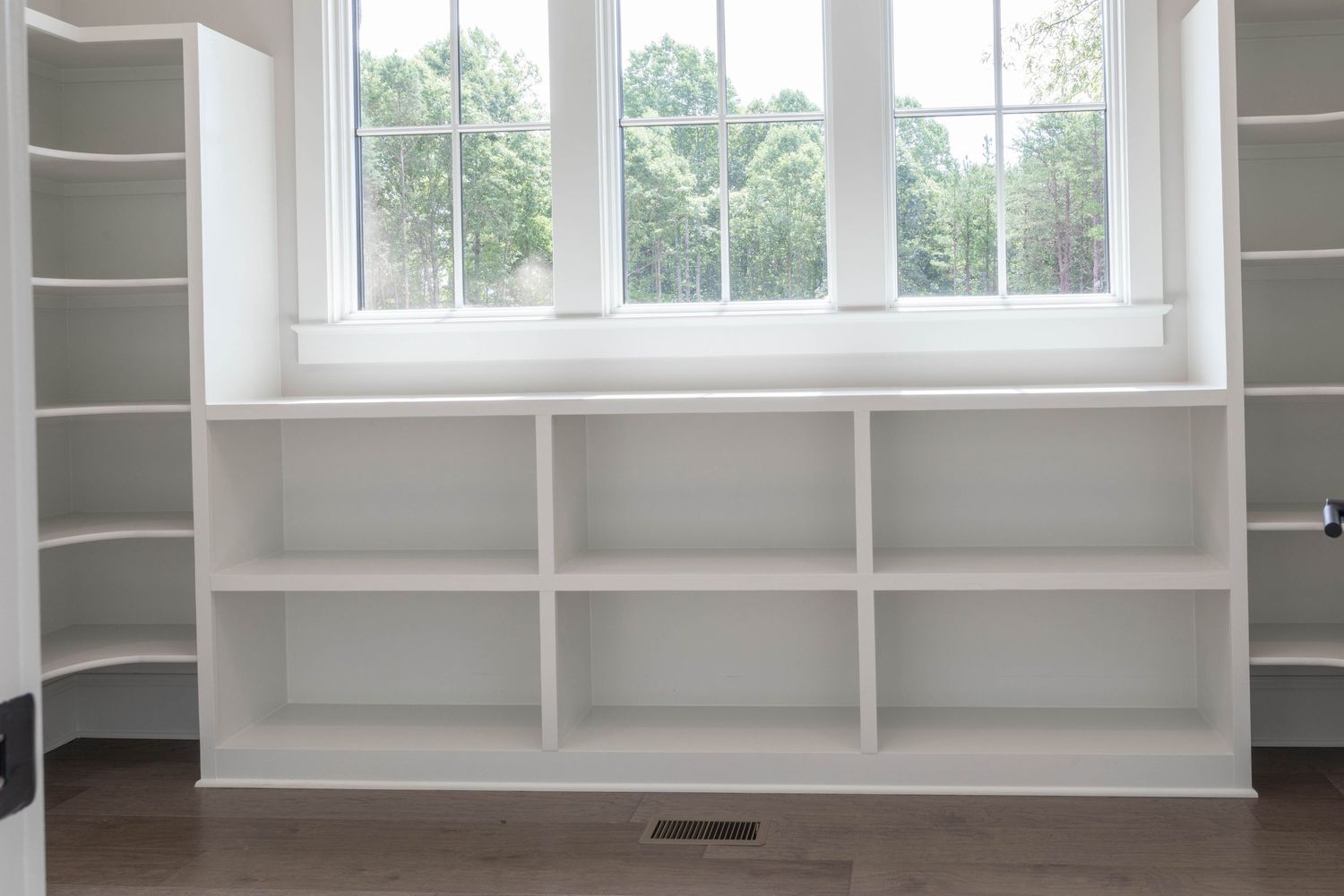 Custom white built-in shelving unit beneath large windows with natural light streaming in.