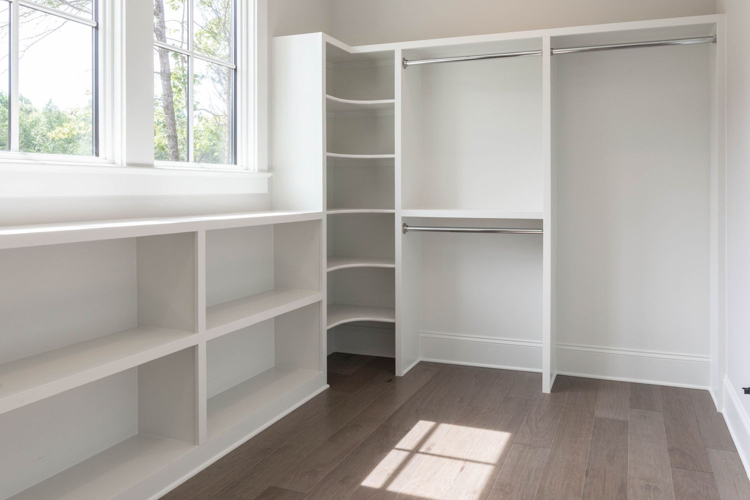 White walk-in closet featuring built-in shelves, hanging rods, and large windows for natural light.