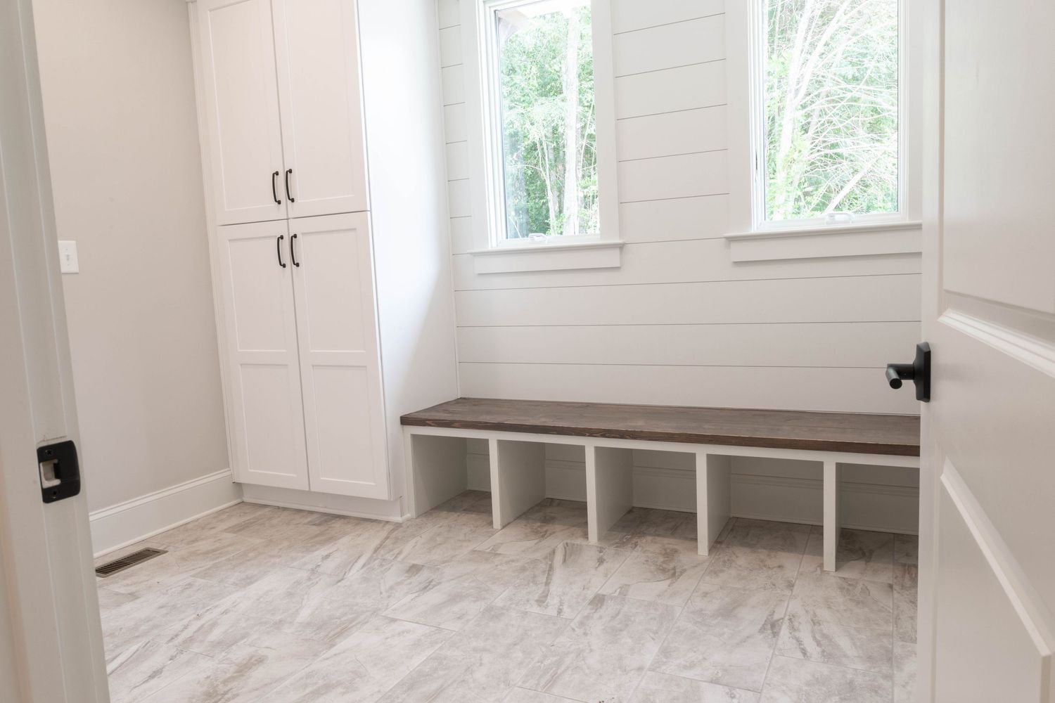 Mudroom with built-in bench seating, white cabinets, and gray flooring beneath windows.