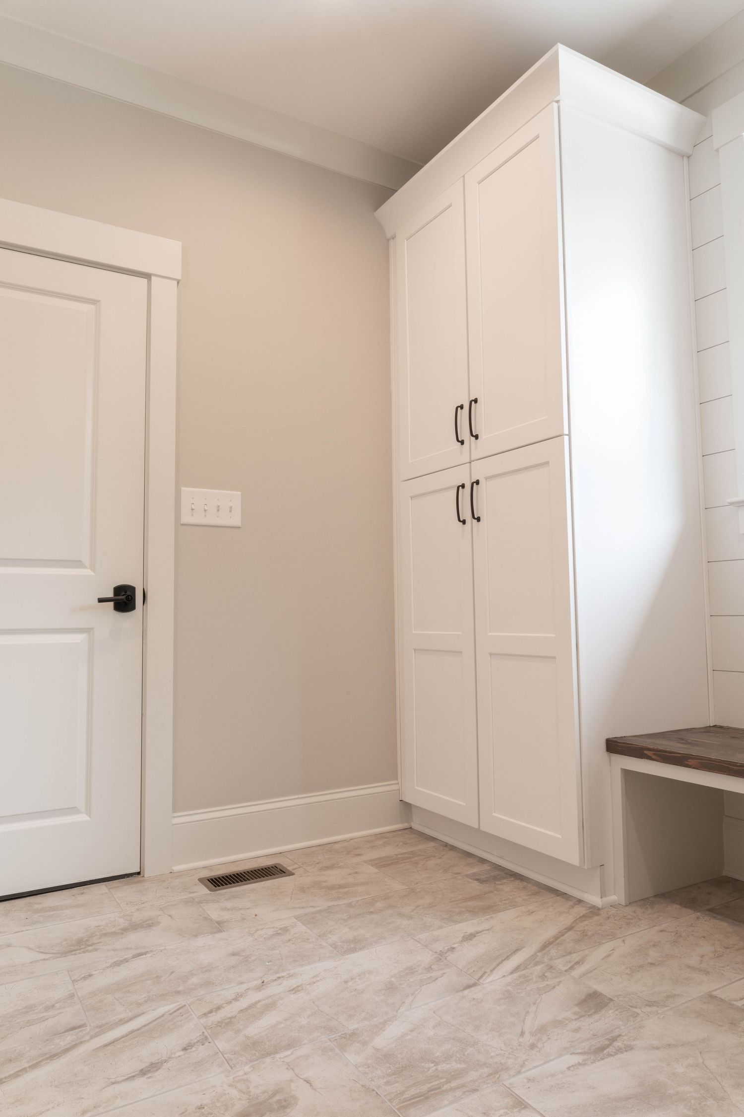 White built-in storage cabinet with wooden bench in a minimalist mudroom with marble-look tile flooring.