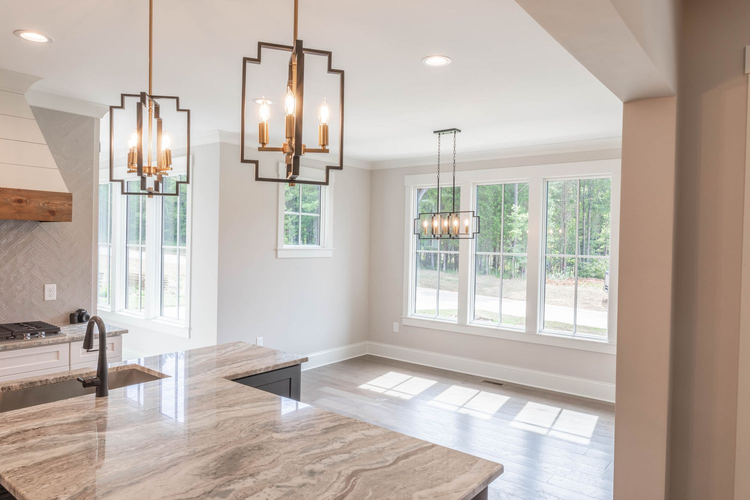 Bright kitchen space featuring geometric pendant lights, marble countertops and large windows with natural lighting.