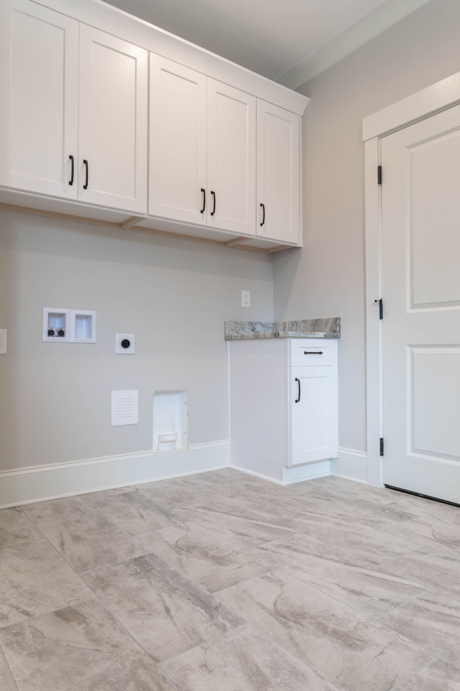 White laundry room with modern cabinetry, built-in appliance space, and grey marble-look tile floors.