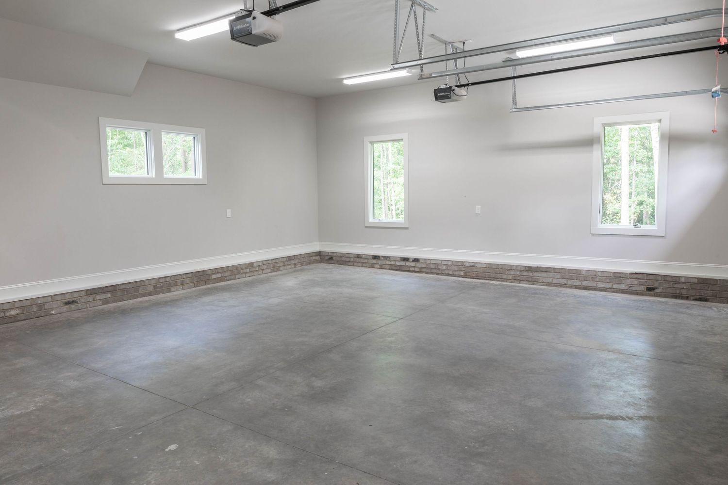 Empty garage interior with white walls, fluorescent lighting, and polished concrete flooring.