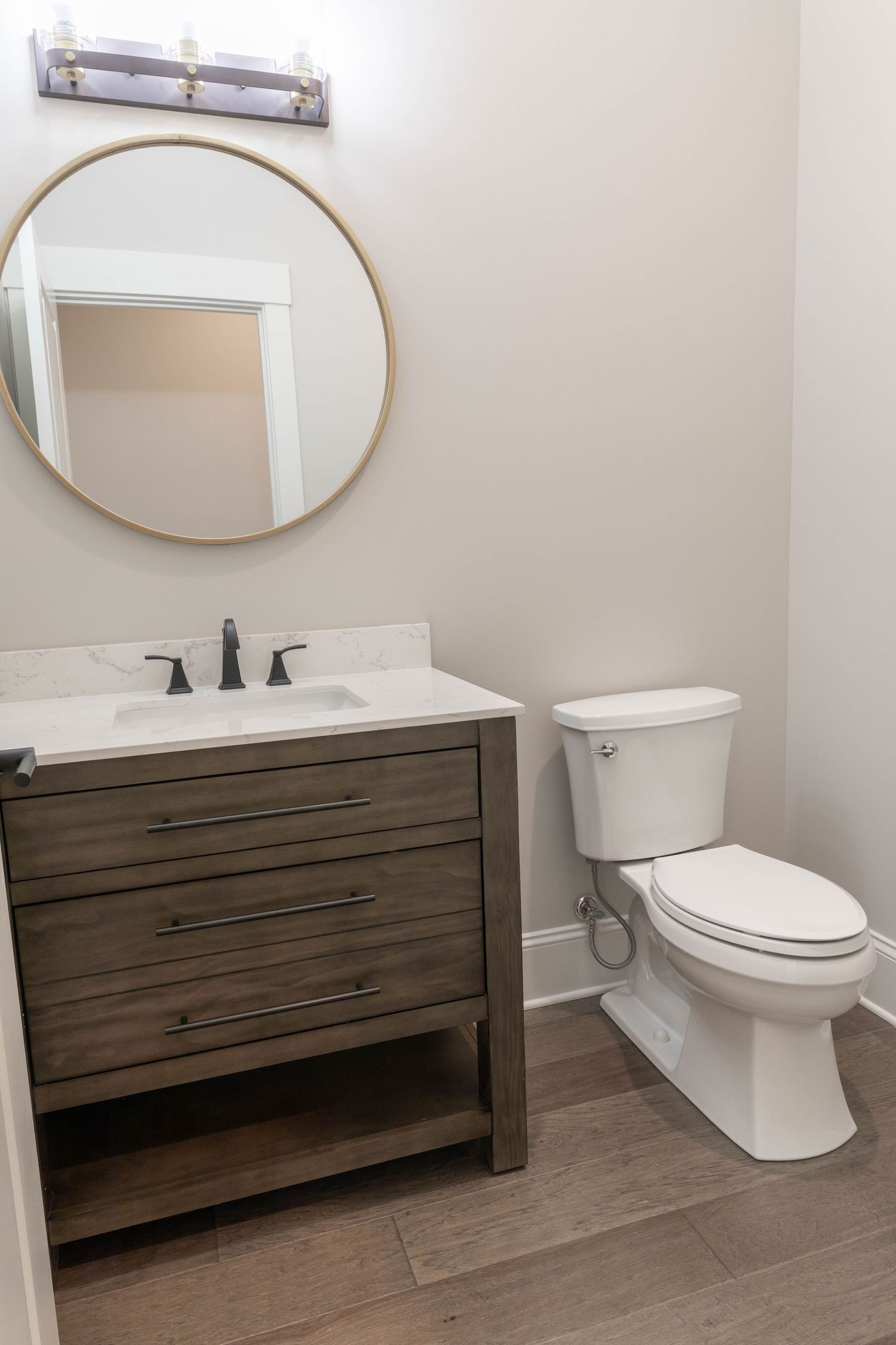 Contemporary bathroom featuring wooden vanity, round mirror, and modern fixtures on grey tile flooring.