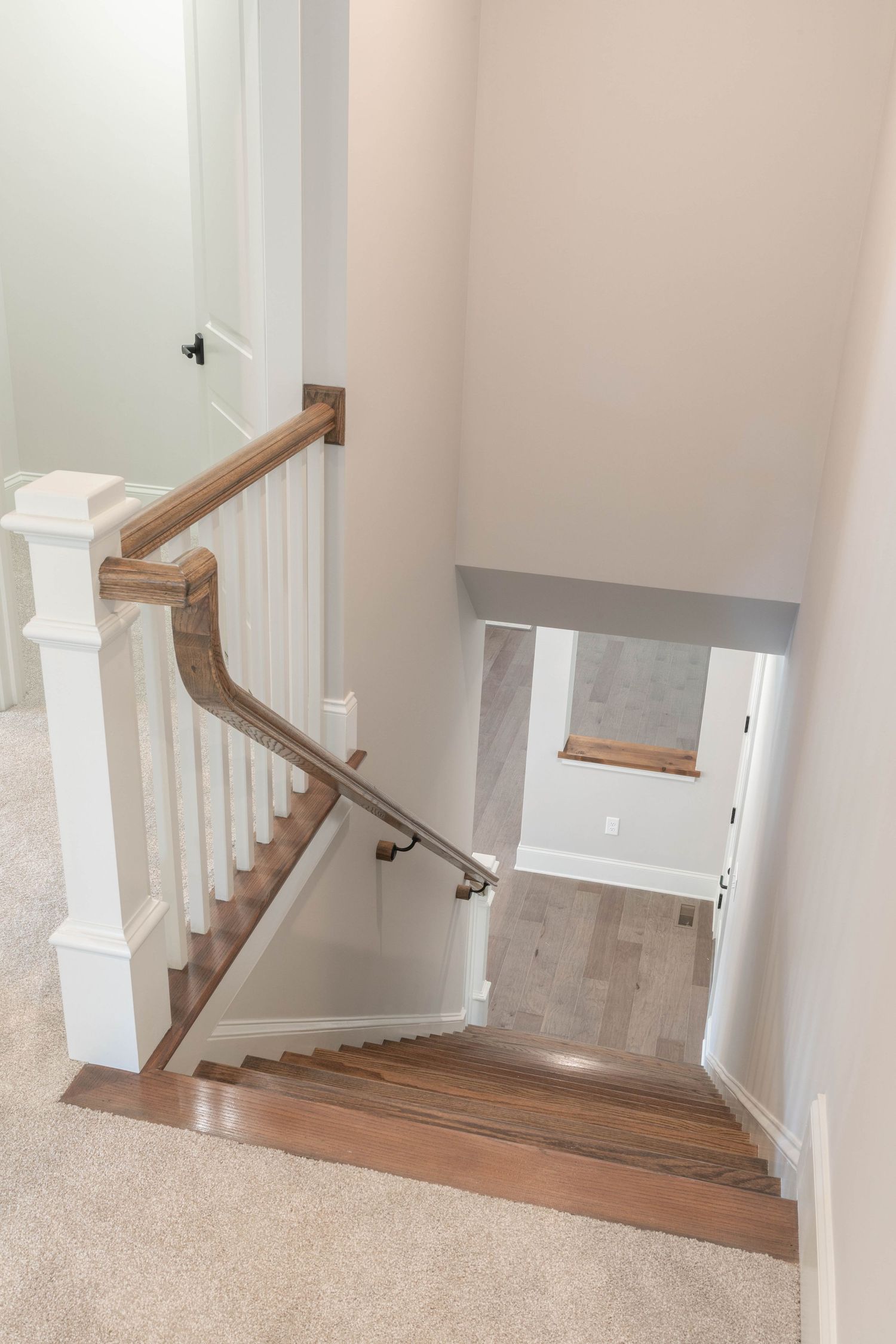 Elegant staircase with white spindles, wooden handrail, and carpeted steps leading downstairs.