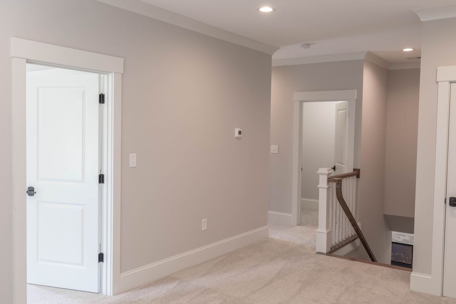Bright hallway with white doors, beige walls, and plush carpet flooring.