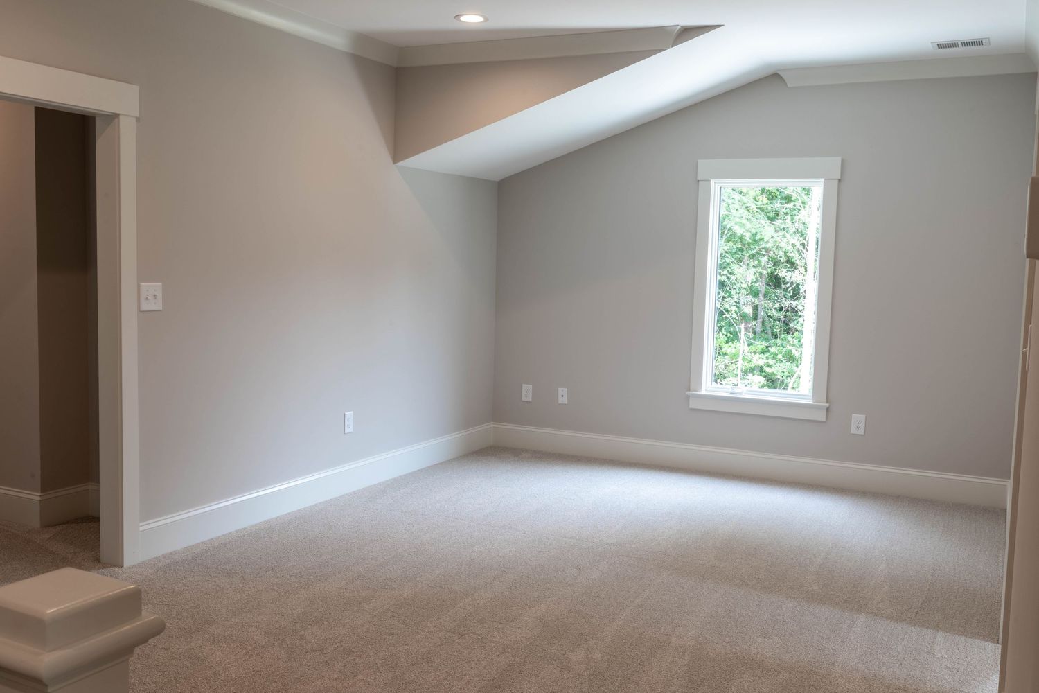 Modern empty room with angled ceiling, neutral walls, and plush carpet flooring.