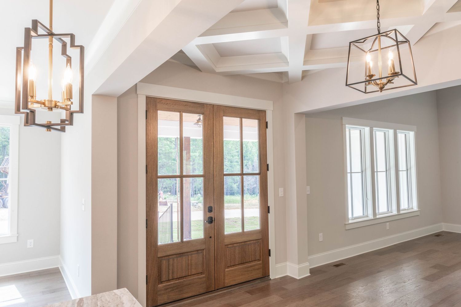 Elegant entryway with wooden French doors, geometric pendant lights and coffered ceiling details.