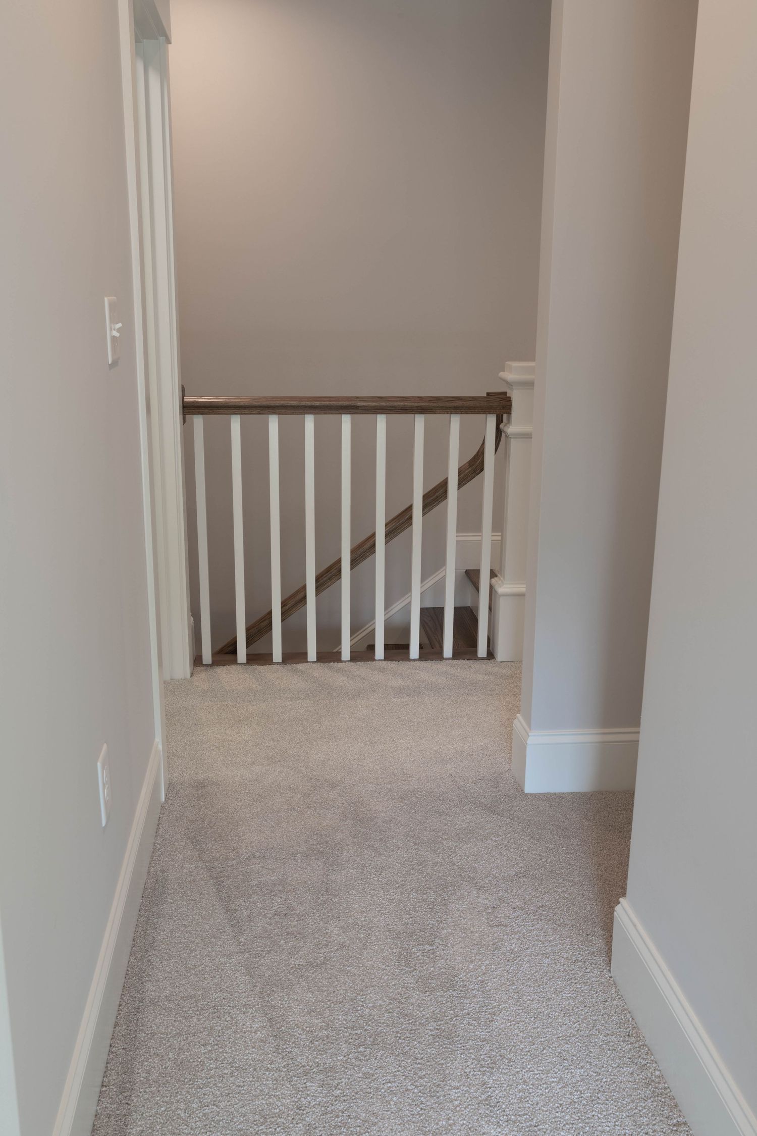 Carpeted hallway with white trim and wooden banister leading to staircase.