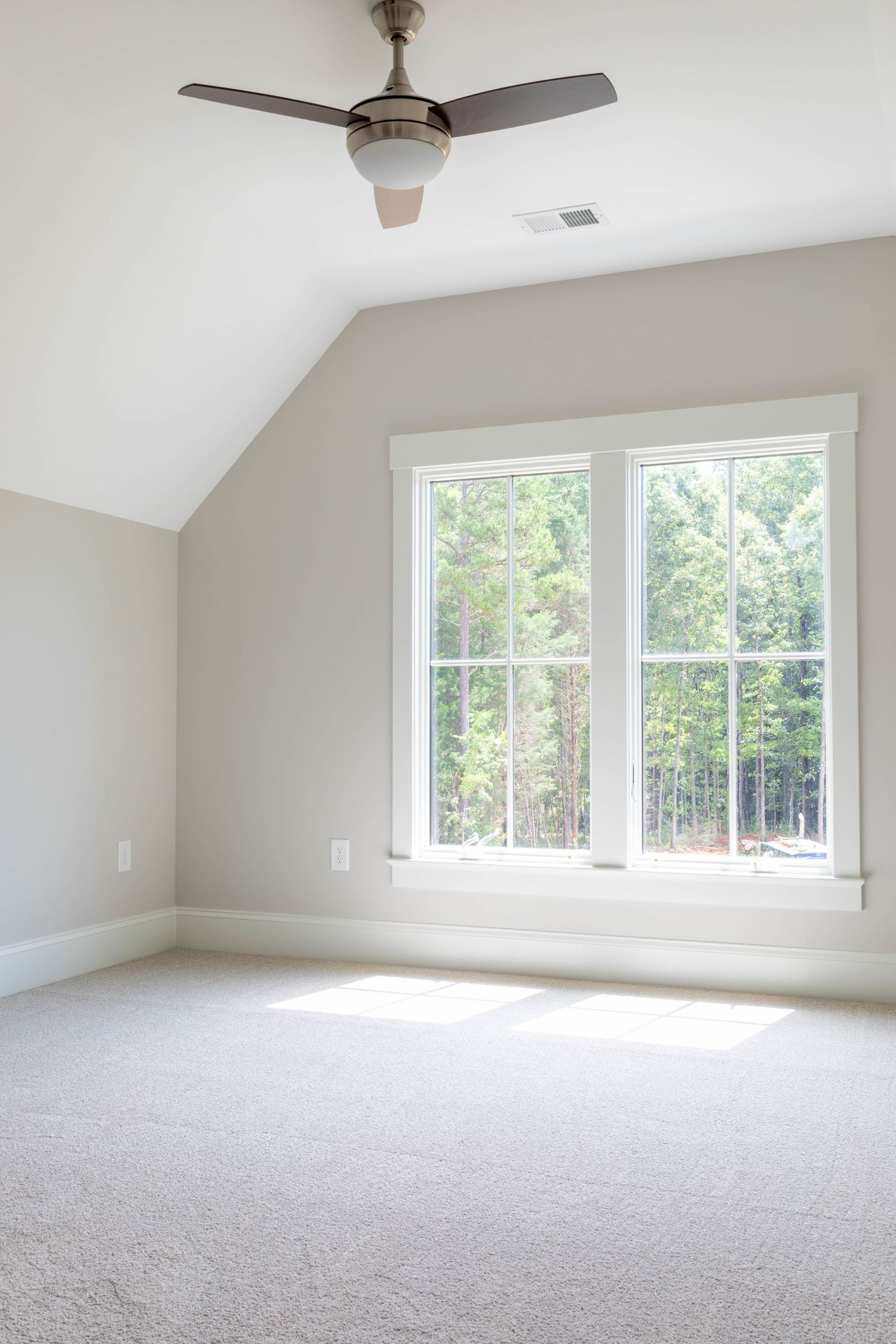 Bright bedroom with vaulted ceiling, ceiling fan, and large double-hung window with forest views.