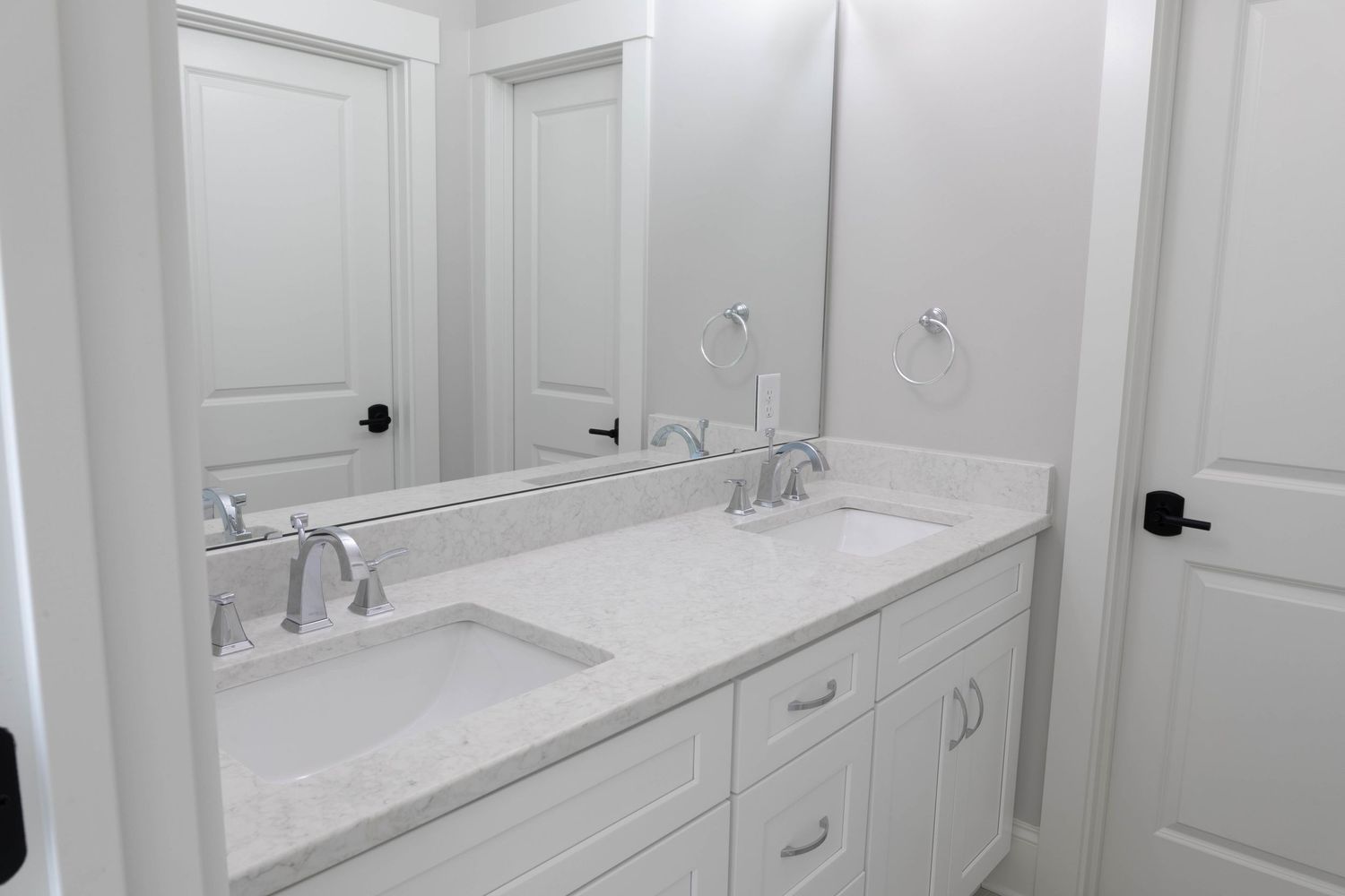 Clean white bathroom featuring double vanity with chrome faucets and large mirror.